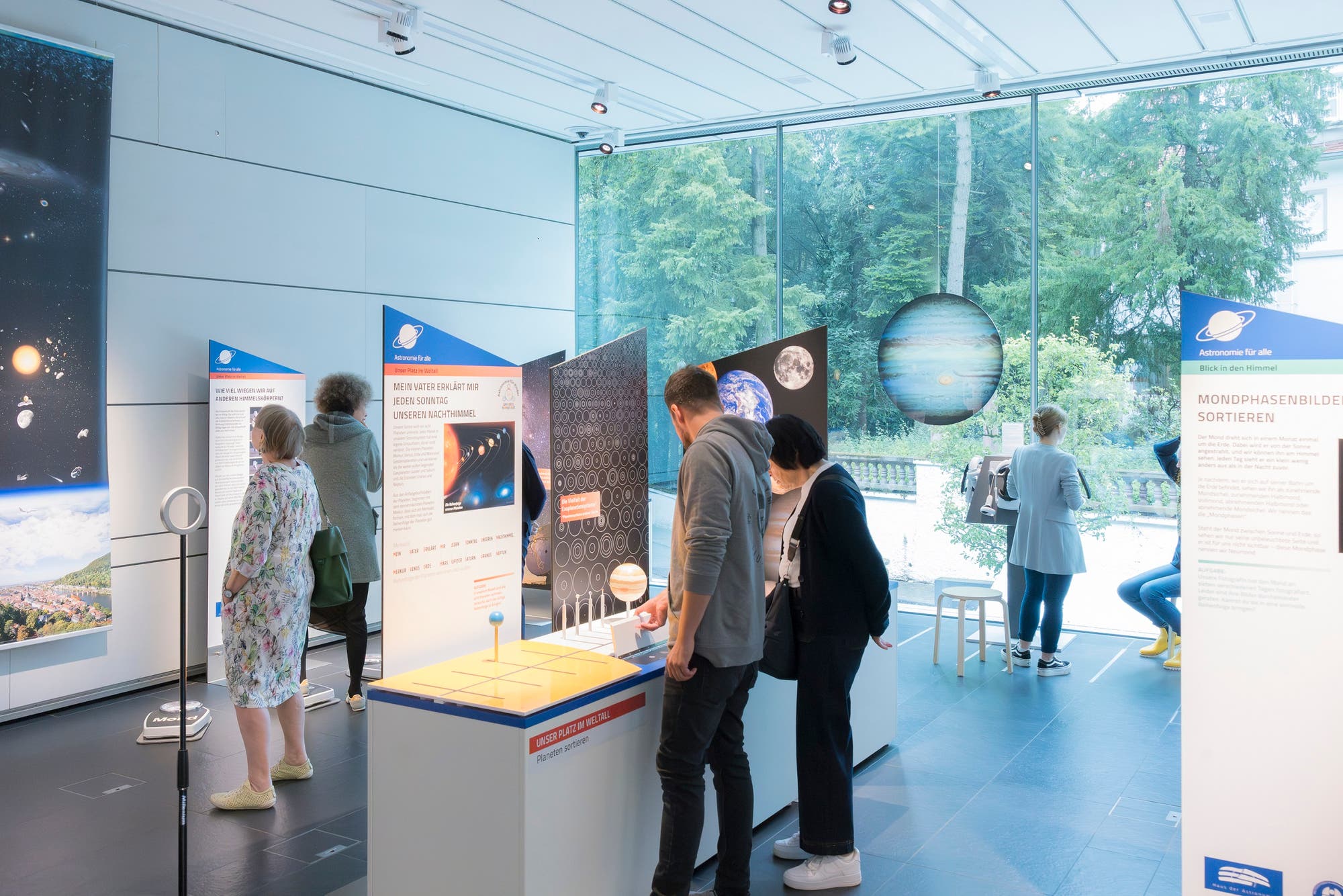 Foto der Ausstellung »Astronomie für alle«, auf der einige Exponate und Besucherinnen und Besucher zu sehen sind.