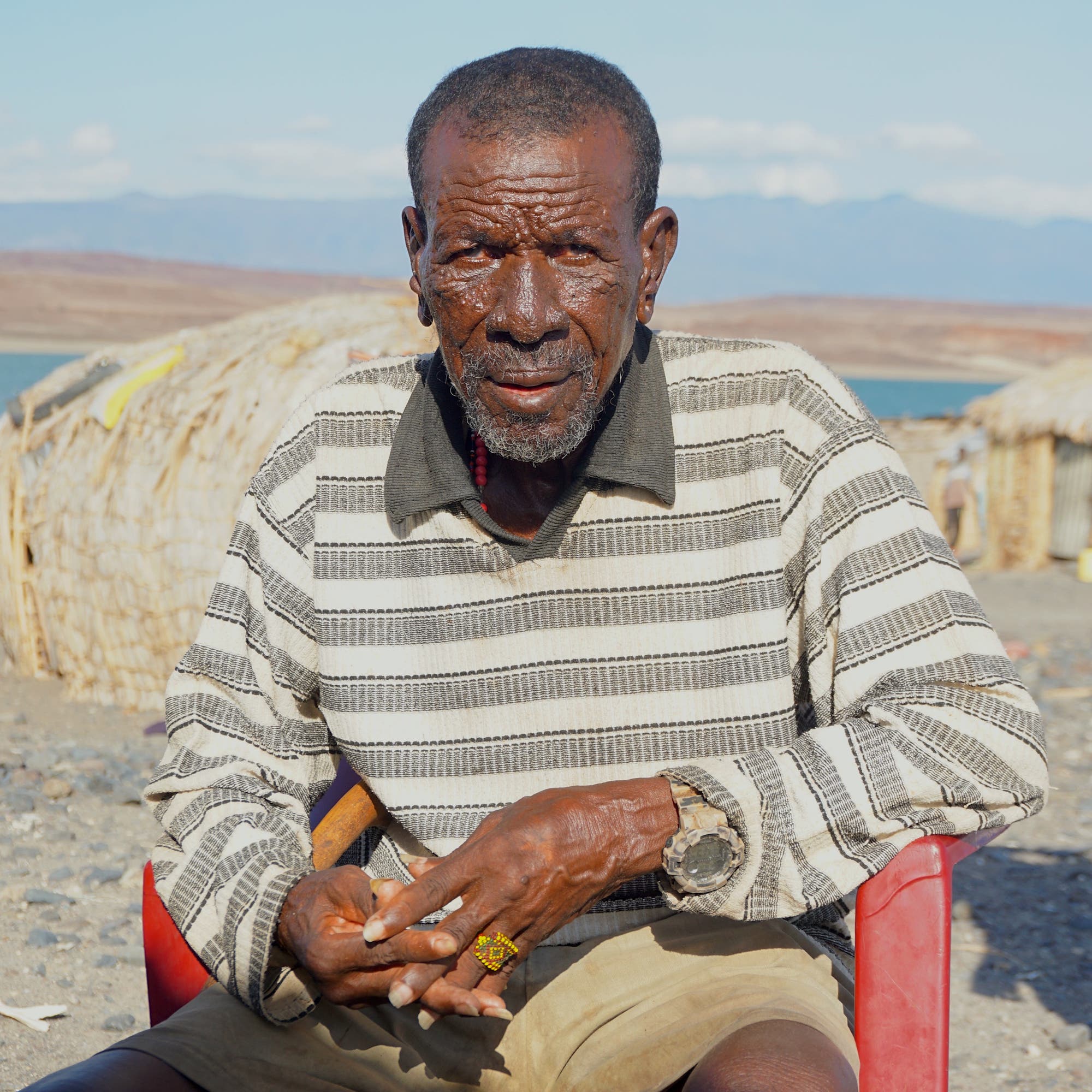 Ein El-Molo-Ältester sitzt auf einem roten Plastikstuhl am Turkanasee.