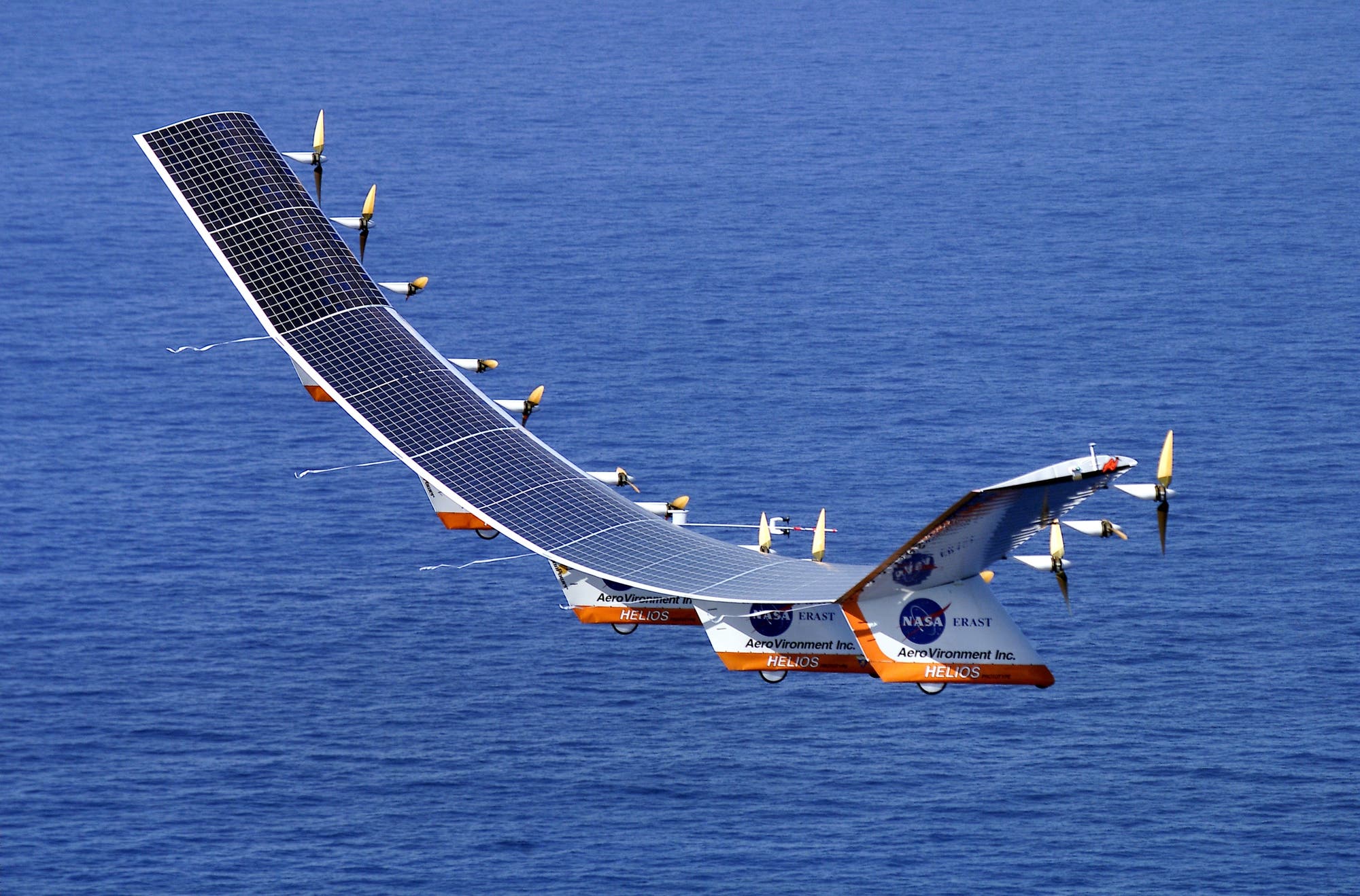 Ein Leichtflugzeug mit großer Spannweite, dessen Flügeloberseite mit Solarzellen bedeckt ist, fliegt über den Ozean. Die Flügel biegen sich unter dem Gewicht des Fluggeräts stark durch.