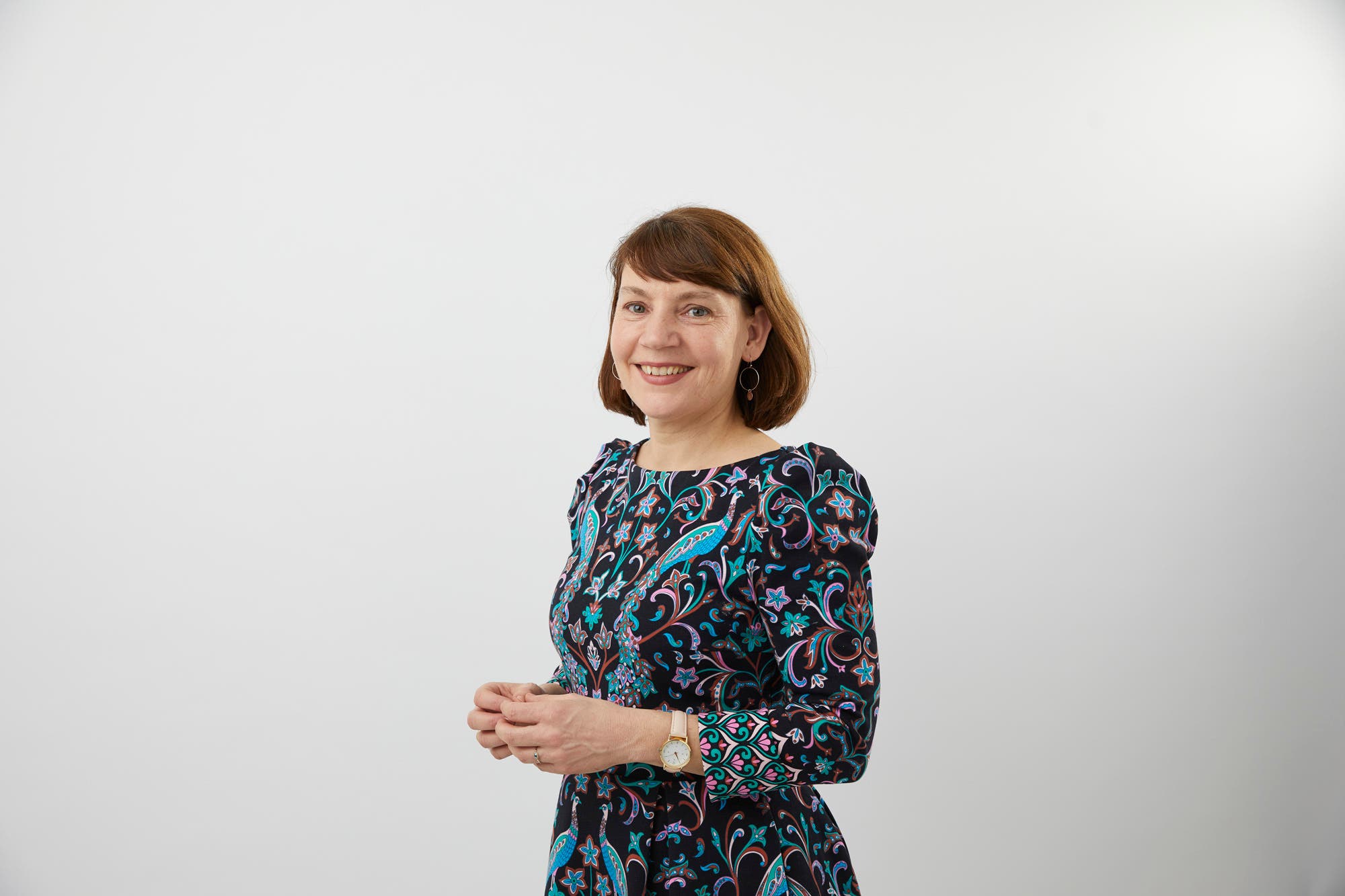 Die Psychologin Eva Hoch steht in einem bunten Kleid vor einem hellen Hintergrund. Ihr Haar ist braun, sie trägt es mit Pony zum Bob geschnitten. Sie lächelt freundlich in die Kamera.