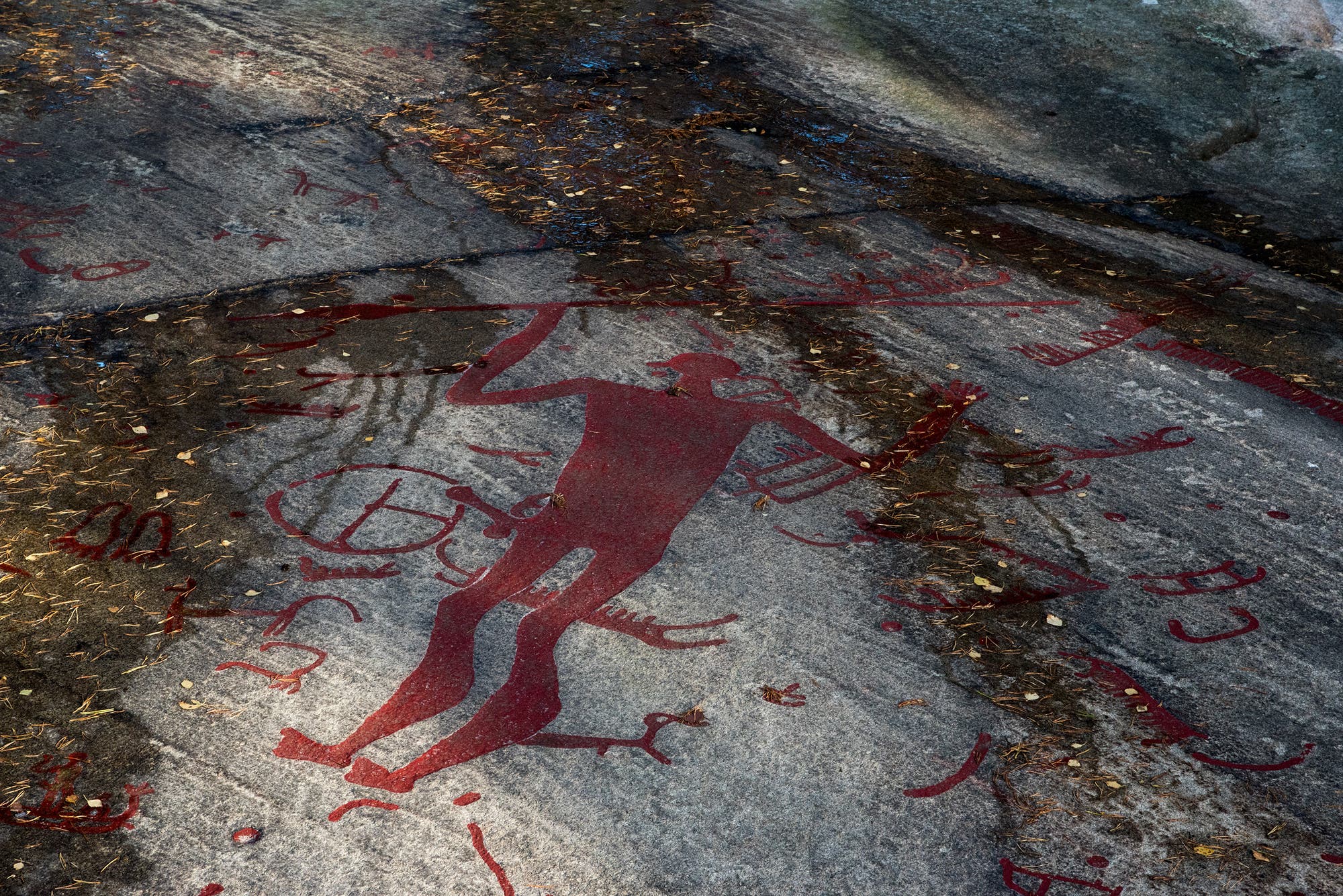 Eine rot ausgemalte Menschenfigur mit einem Speer in der Hand und einem angeblichen Schwertgriff an der Hüfte. An dem Schwertgriff hängt unten ein kugeliger Anhang und der Rest des Schwerts ist im Bild auch nirgends zu sehen. 