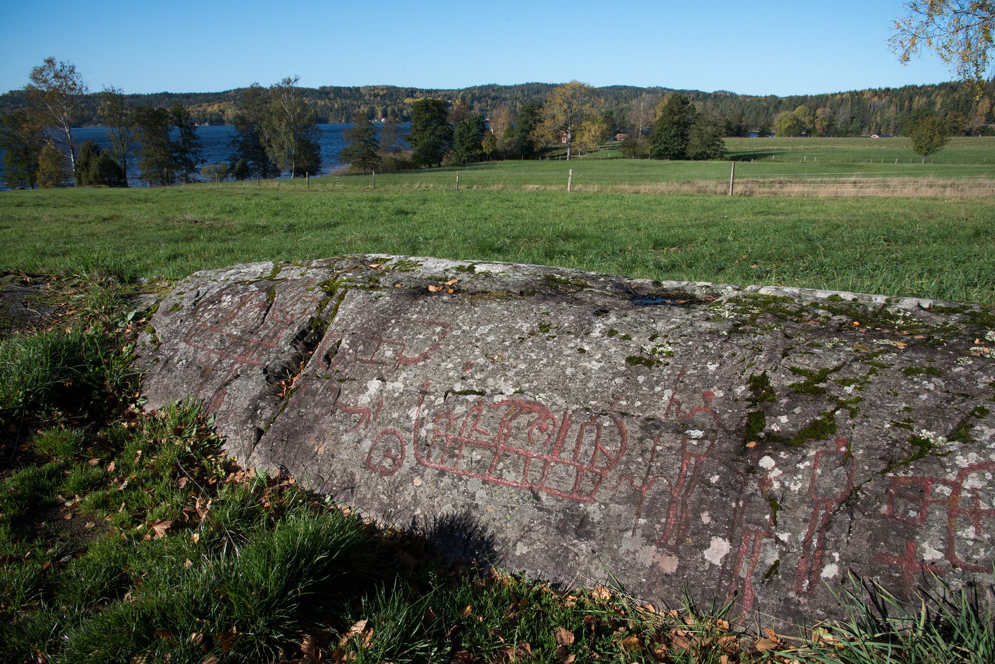 Rot ausgemalte Petroglyphen auf einem Felsen in der Landschaft.