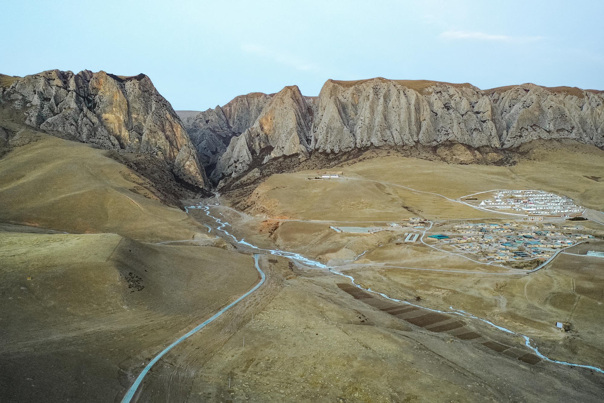 Blick auf das Bergmassiv mit der Baishiya-Höhle am Rand des Ganjia-Beckens. Im Vordergrund eine Siedlung.