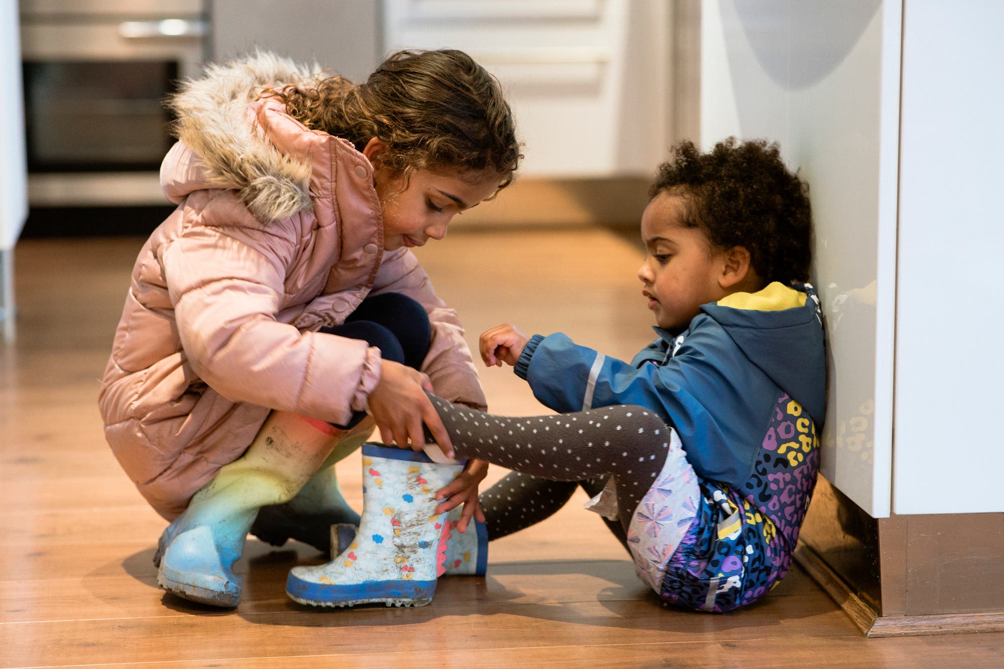 Vorschulkind hilft kleinerem Geschwisterkind beim Gummistiefel anziehen