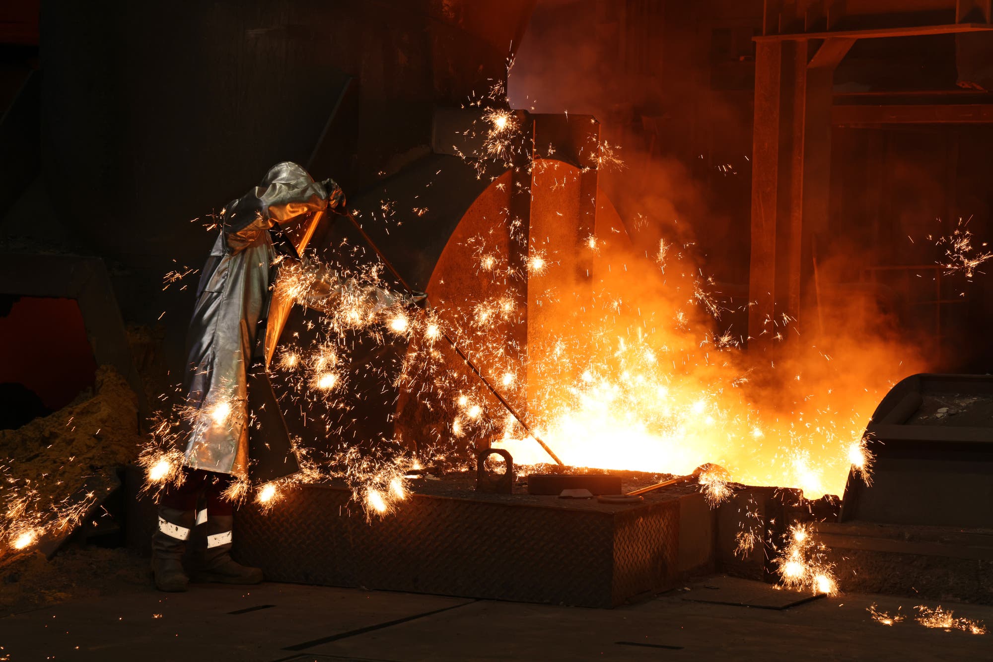 Ein Arbeiter in einer Schutzkleidung steht in einer Gießerei und überwacht den Guss von geschmolzenem Metall. Funken fliegen in alle Richtungen, während das glühende Metall in eine Form gegossen wird. Die Szene ist von intensiver Hitze und Licht geprägt, was die gefährlichen Arbeitsbedingungen in der Metallverarbeitung verdeutlicht.