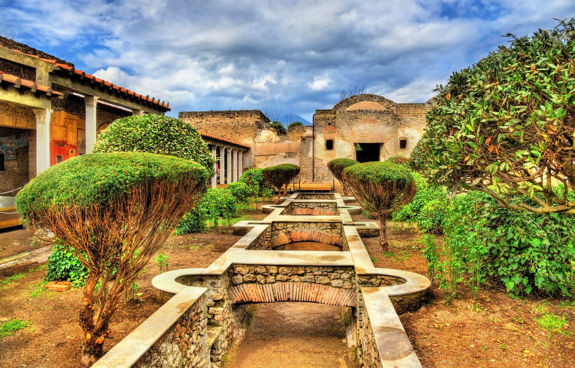 Garten im Anwesen der Julia Felix in Pompeji mit Kanal und Brücken. Im Garten stehen Bäume und Sträucher.