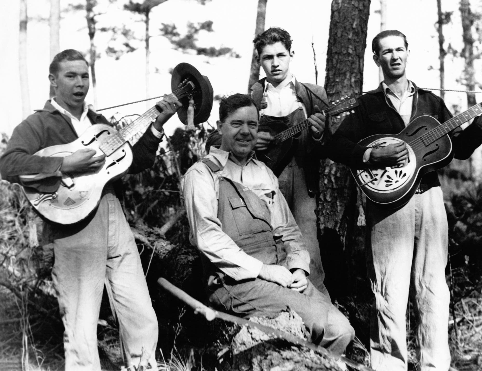 Eine Gruppe von vier Männern befinden sich in einem Wald. Drei von ihnen stehen und spielen Gitarre, während der vierte Mann, Huey Long, in der Mitte sitzt und lächelt. Alle inklusive dem Politiker tragen Arbeitskleidung und Latzhosen, wie sie für das Bild des "Südstaaten-Rednecks" kennzeichnend sind.