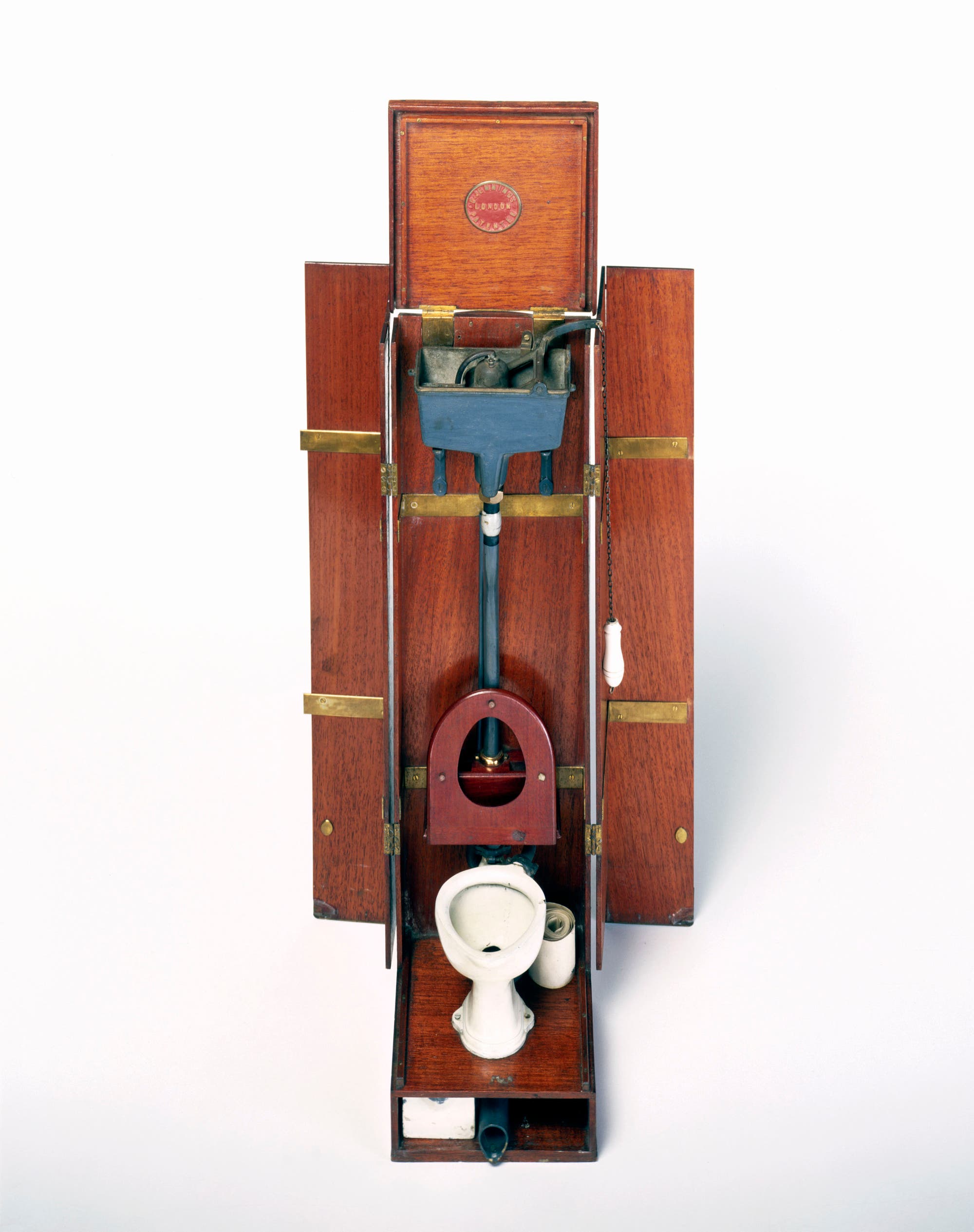 Ein Modell einer Toilette mit einem hölzernen Gehäuse aus der Zeit um 1900. Das Modell zeigt die Mechanik eines Spülkastens, der über ein Rohr mit der Toilettenschüssel verbunden ist. Ein Kettenzug ist an der rechten Seite sichtbar. Das Design veranschaulicht die Funktionsweise früher Sanitärtechnik.