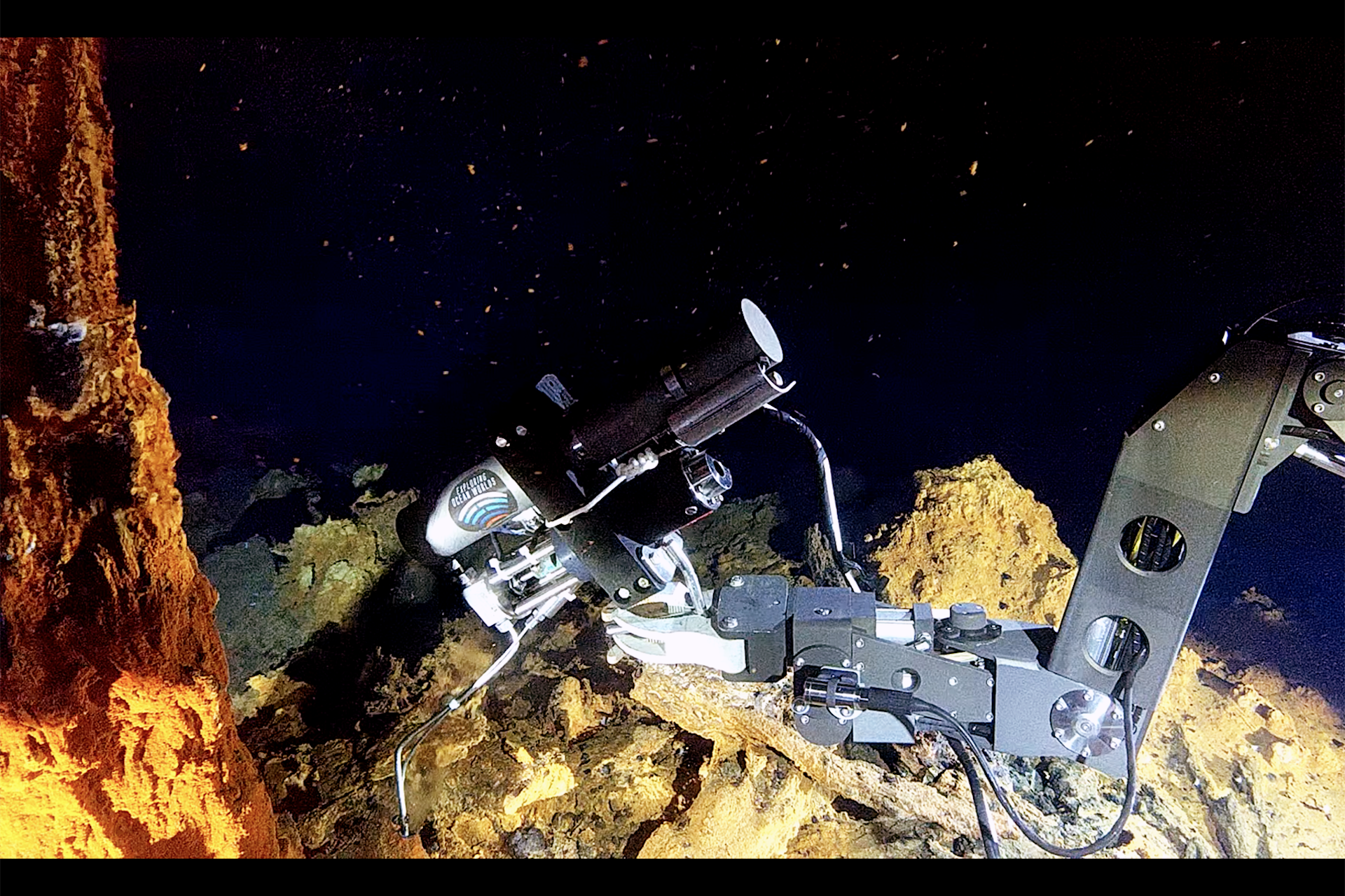 ein Robotergreifarm neben einem Schwarzen Raucher am Meeresboden