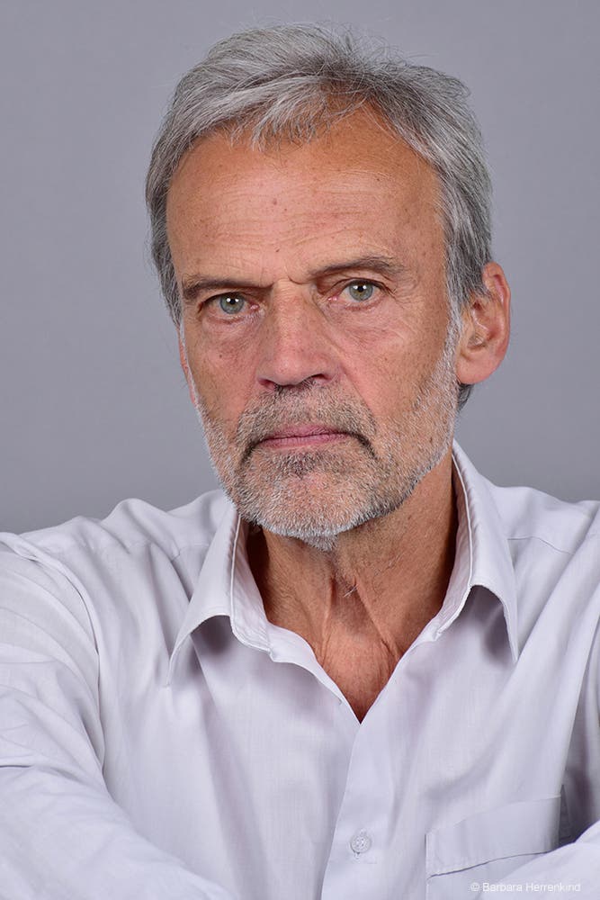 Ein Porträtfoto von Horst Bredekamp. Er trägt ein helles Hemd mit geöffnetem Kragen und blickt ernst in die Kamera.