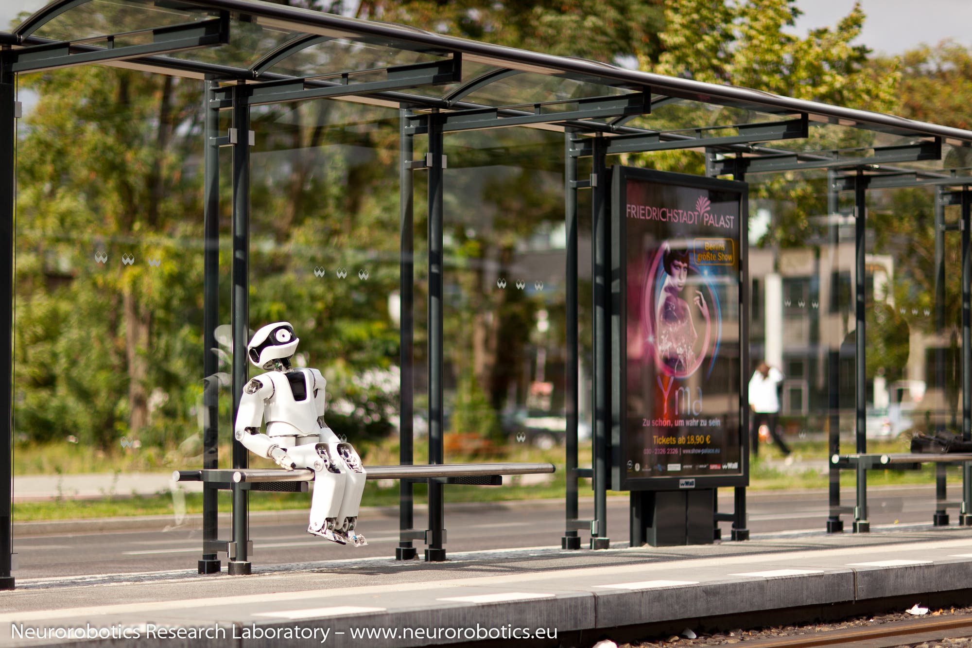 Roboter Myon sitzt an einer Bushaltestelle
