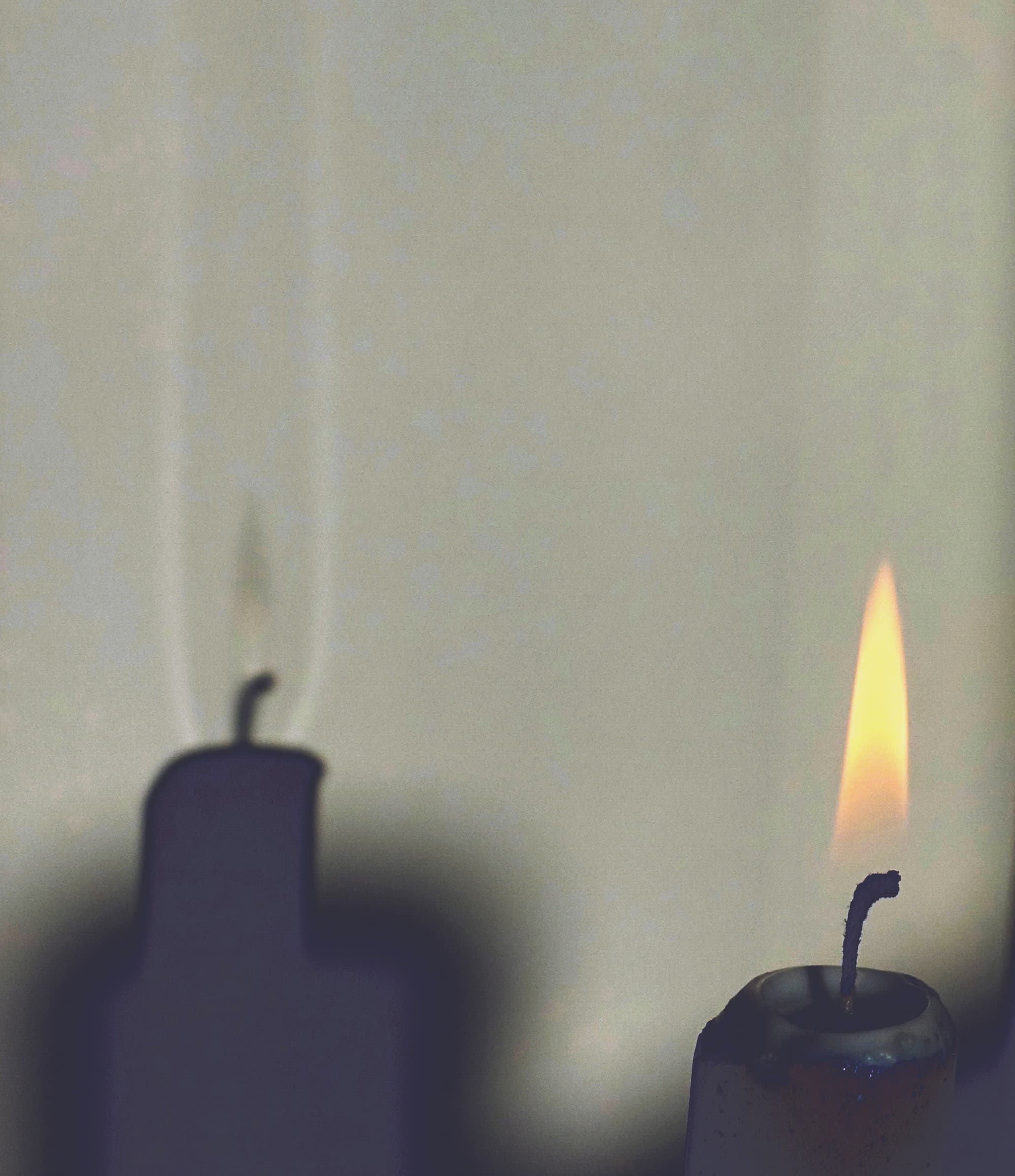 Eine brennende Kerze steht im Sonnenlicht. Auf der weißen Wand ist zu erkennen, dass der Schatten der Flamme von zwei senkrechten Lichtbändern eingerahmt wird. Oberhalb des Dochts ist ein ähnlich heller Fleck.
