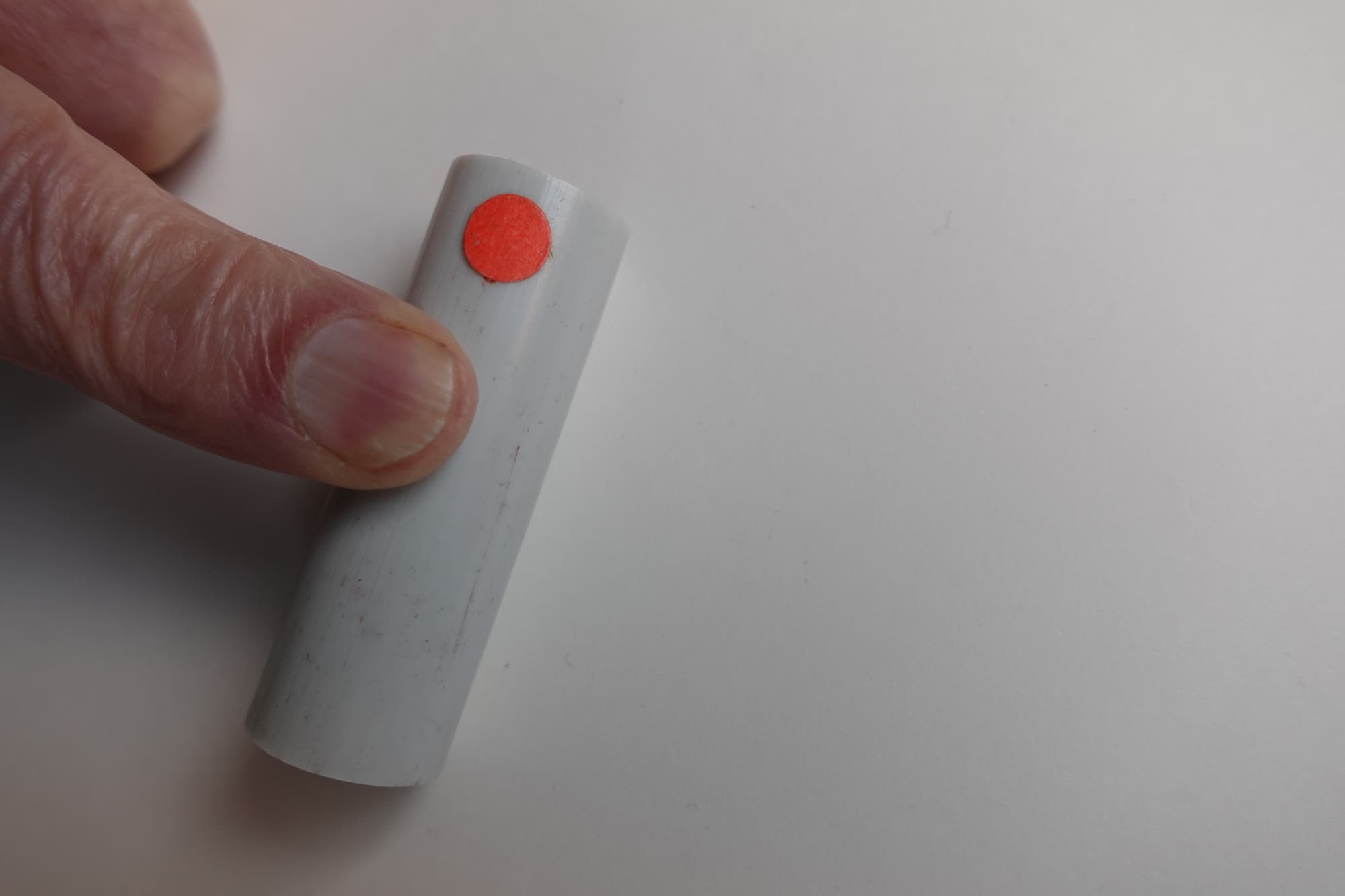 Ein Finger drückt auf ein Stück Plastikrohr, das mit einem roten Punkt beklebt ist.