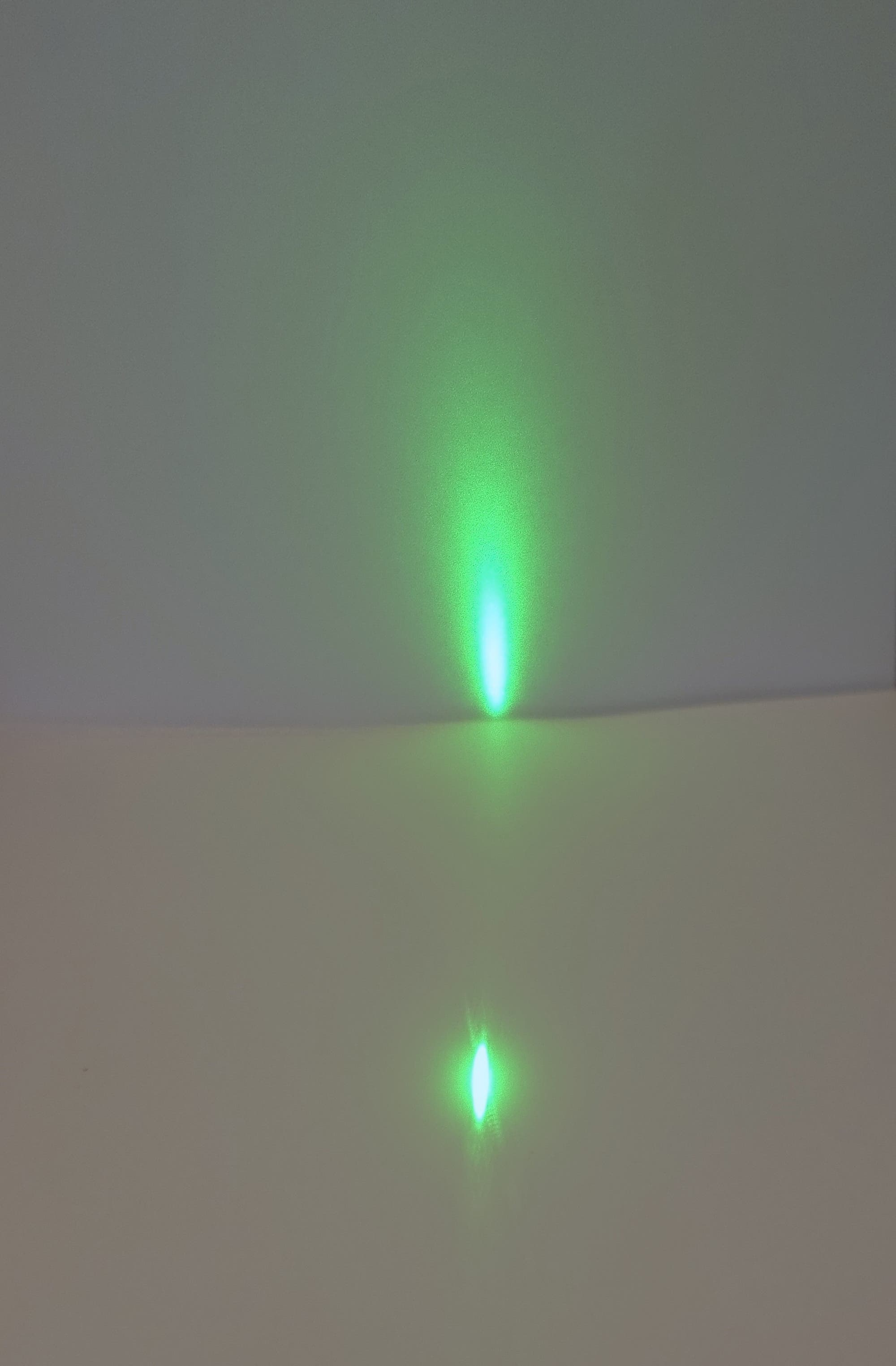 Der Strahl eines Laserpointers wird beim schrägen Einfall auf einem Blatt Papier von diesem an einen Schirm reflektiert