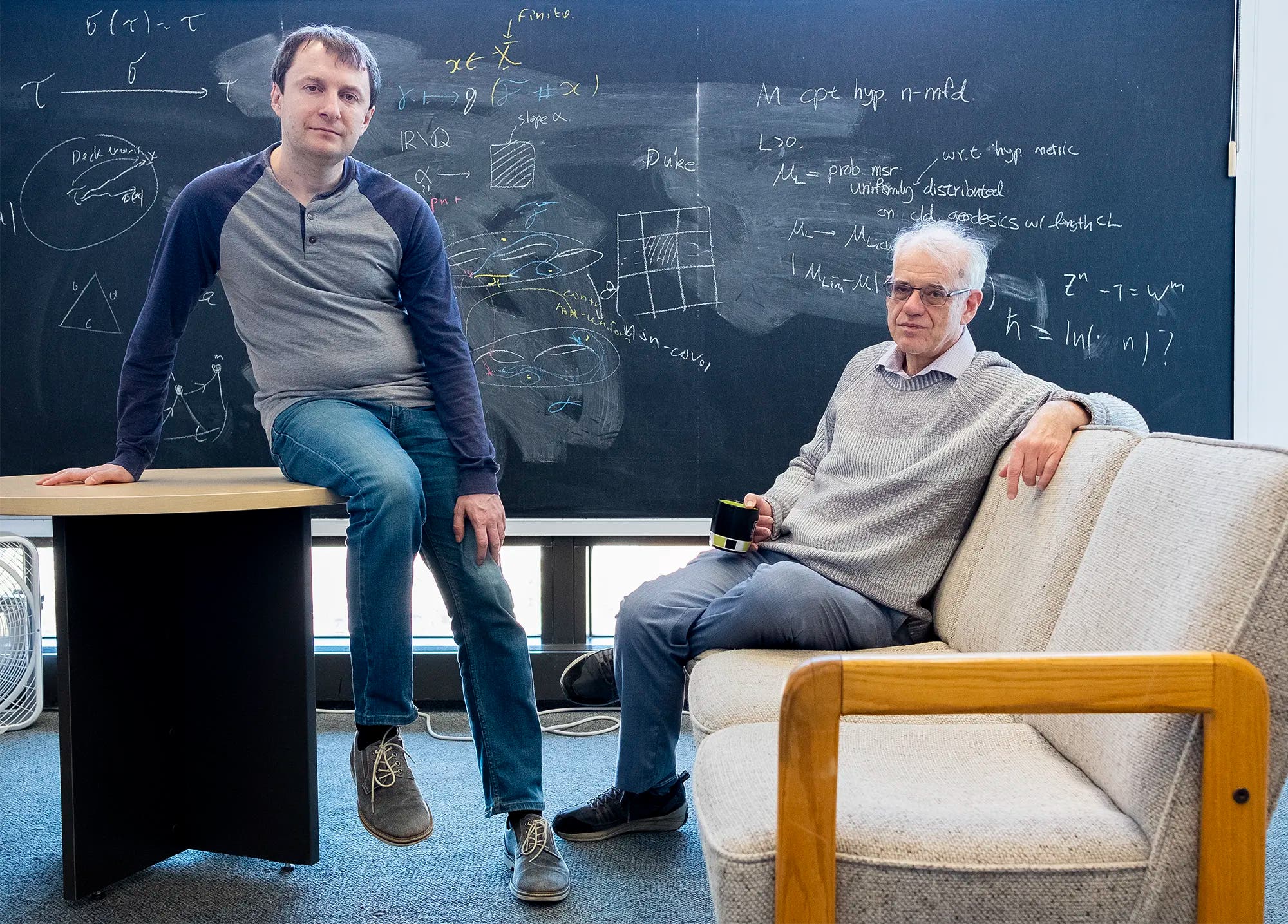 Ein Bild mit den beiden Forschern in einem Raum mit einer Tafel