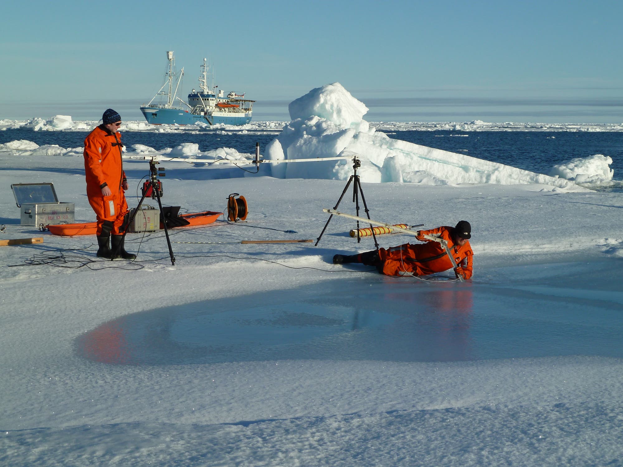 Polarforscher untersuchen eine Schmelzwasserpfütze auf dem Eis