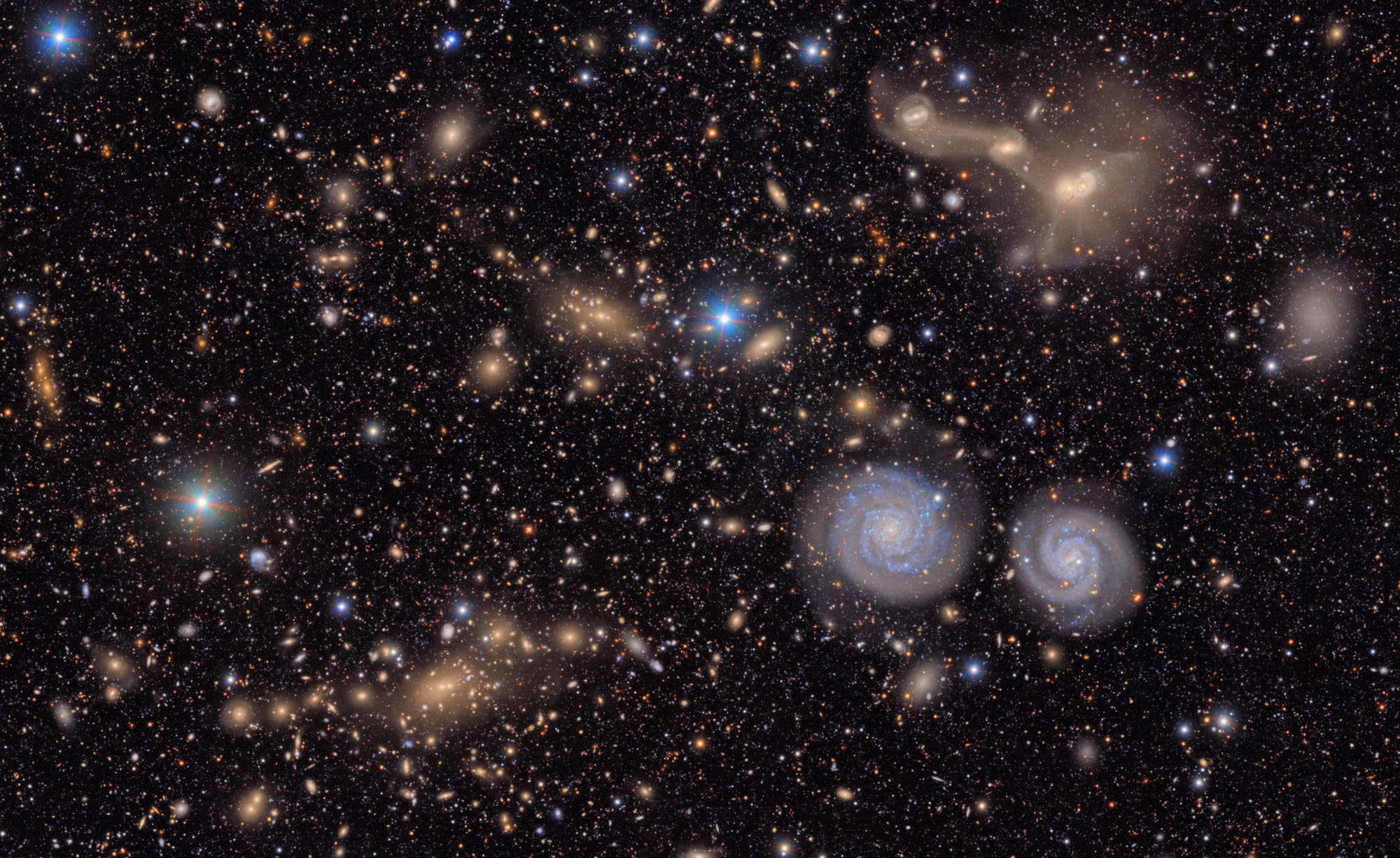 Una imagen impresionante del universo con numerosas galaxias y estrellas que brillan en diferentes colores. Se encuentran dos galaxias espirales extraordinarias en el área inferior derecha de la imagen. El fondo es profundo, lo que subraya el brillo de las galaxias y las estrellas. No hay personas ni texto disponibles en la foto.