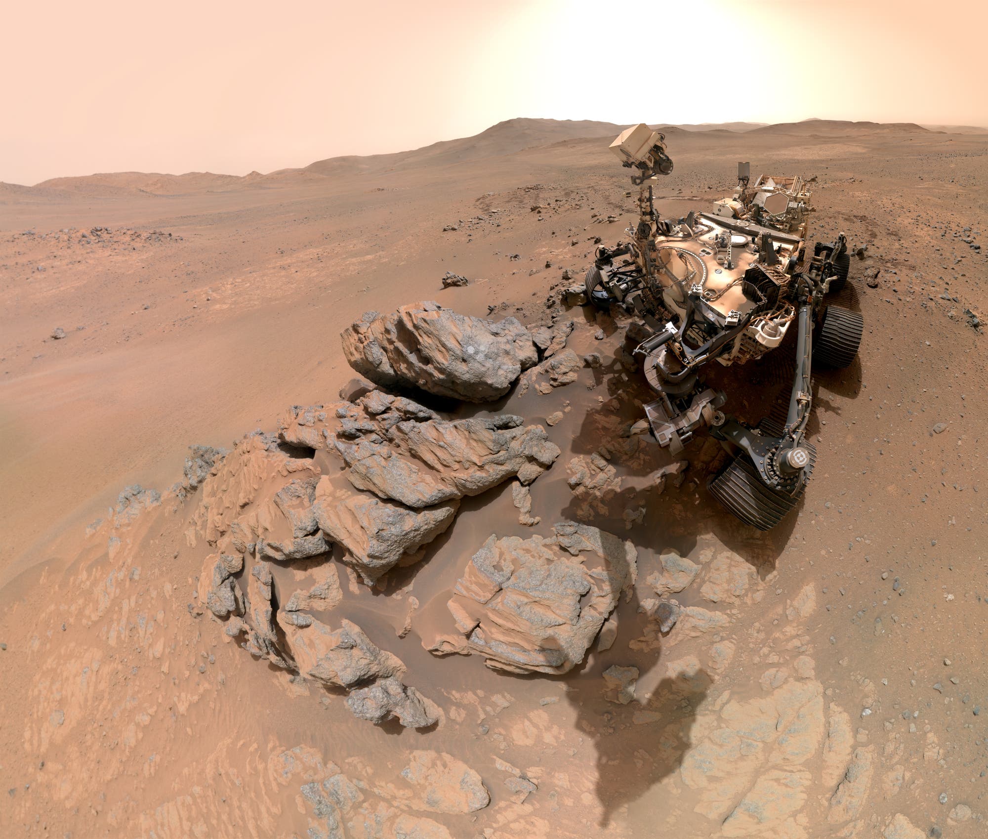Ein Mars-Rover steht auf einer felsigen, sandigen Oberfläche des Mars. Der Rover ist teilweise von großen, unregelmäßig geformten Felsen umgeben. Der Himmel ist in einem hellen, staubigen Orange gehalten, typisch für die Marsatmosphäre. Im Hintergrund erstreckt sich eine weite, hügelige Landschaft. Der Rover ist mit verschiedenen wissenschaftlichen Instrumenten ausgestattet, die für die Erkundung und Analyse der Marsoberfläche verwendet werden. Ein Mars-Rover steht auf einer felsigen, sandigen Oberfläche des Mars. Der Rover ist teilweise von großen, unregelmäßig geformten Felsen umgeben. Der Himmel ist in einem hellen, staubigen Orange gehalten, typisch für die Marsatmosphäre. Im Hintergrund erstreckt sich eine weite, hügelige Landschaft. Der Rover ist mit verschiedenen wissenschaftlichen Instrumenten ausgestattet, die für die Erkundung und Analyse der Marsoberfläche verwendet werden.
