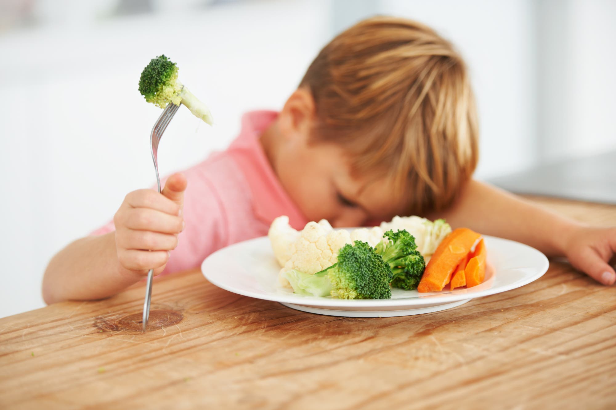 Kind vor einem Teller Gemüse mit einer Gabel in der Hand 