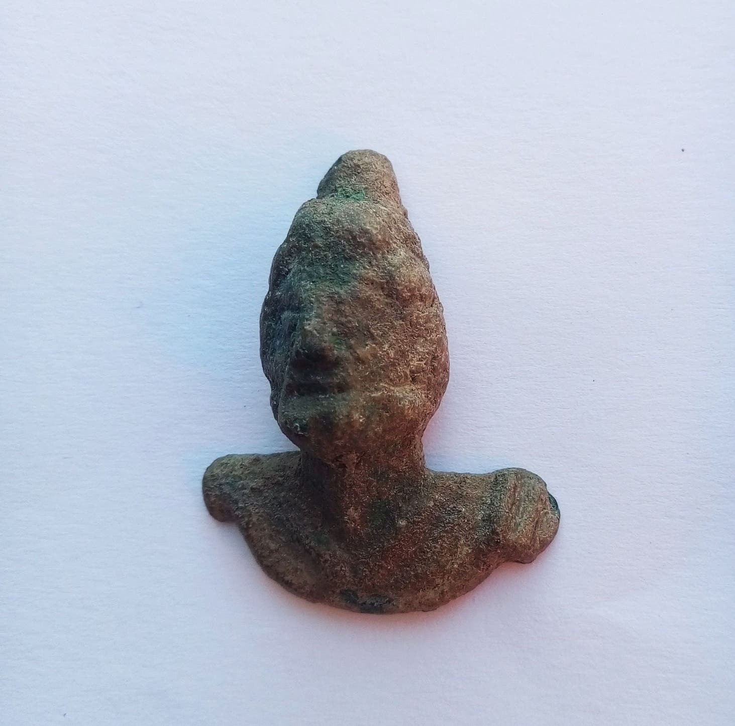 Eine kleine, antike Bronzebüste auf weißem Hintergrund, die eine stilisierte menschliche Figur darstellt. 