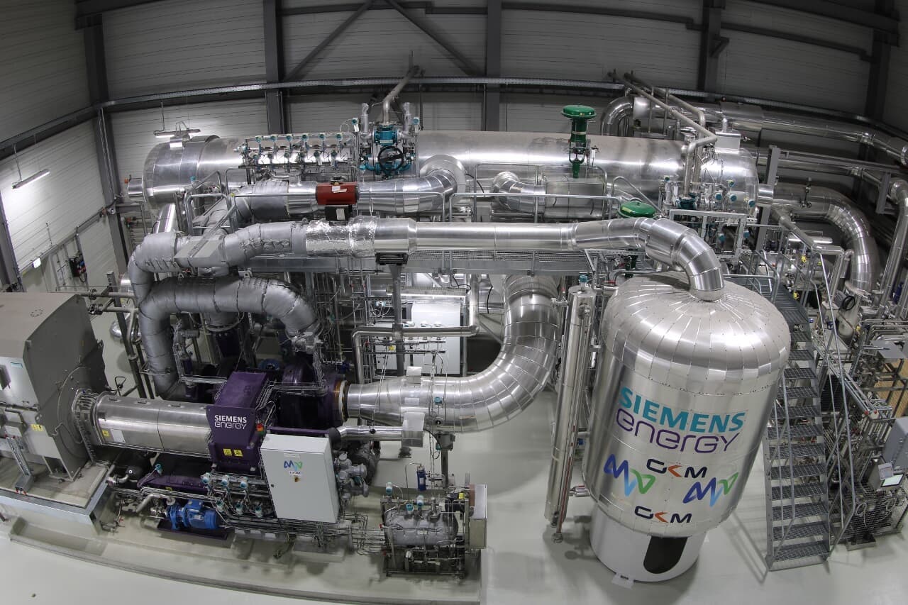 Eine industrielle Anlage mit zahlreichen silbernen Rohren und Tanks, die in einem großen Raum installiert sind. Es handelt sich um eine Großwärmepumpe zur Nutzung von Flusswärme.