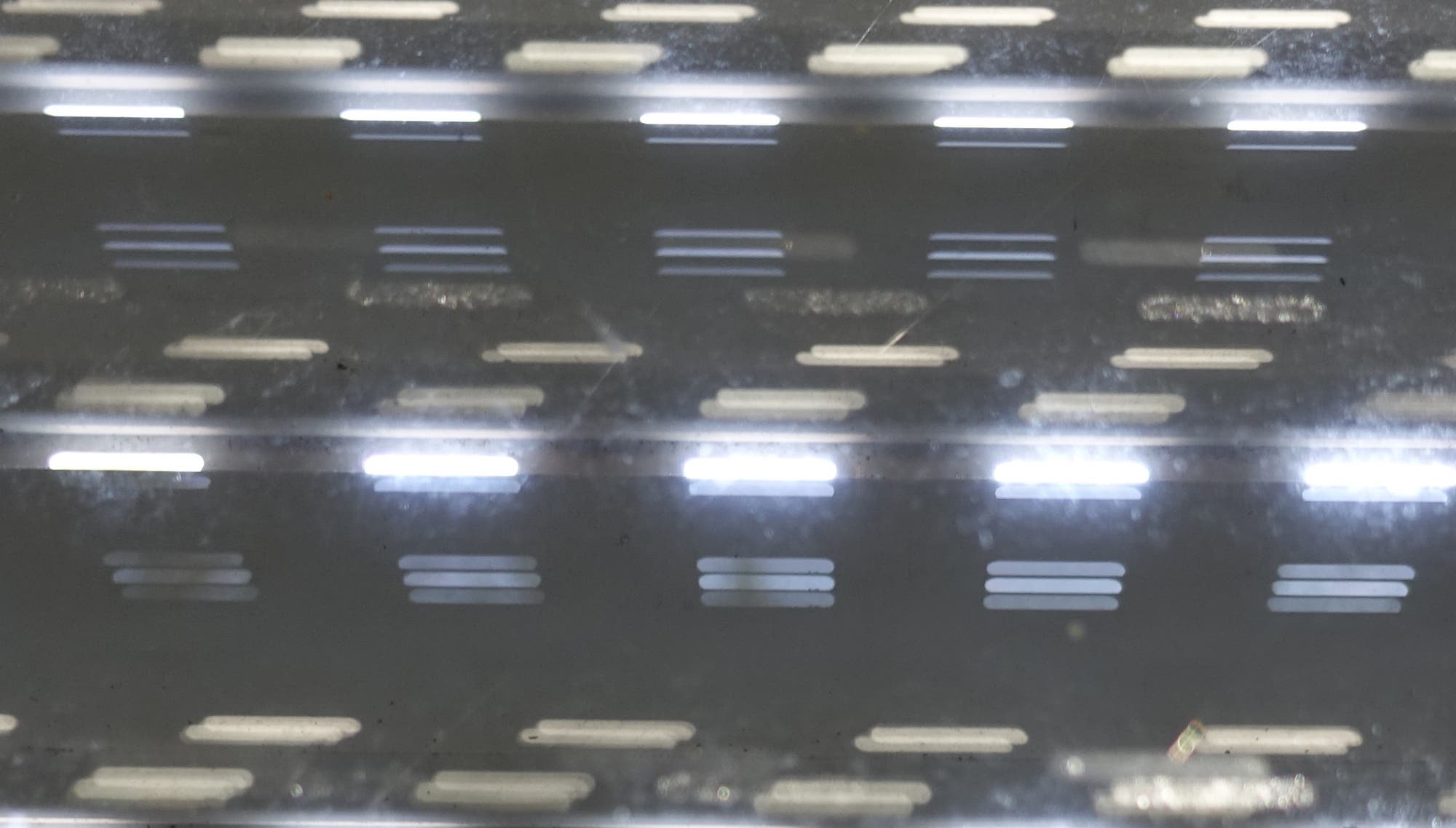 Die Öffnungen zwischen den Lamellen einer Jalousie werden von Licht durchstrahlt und erzeugen zahlreiche helle Streifen (Ausschnittsbild).