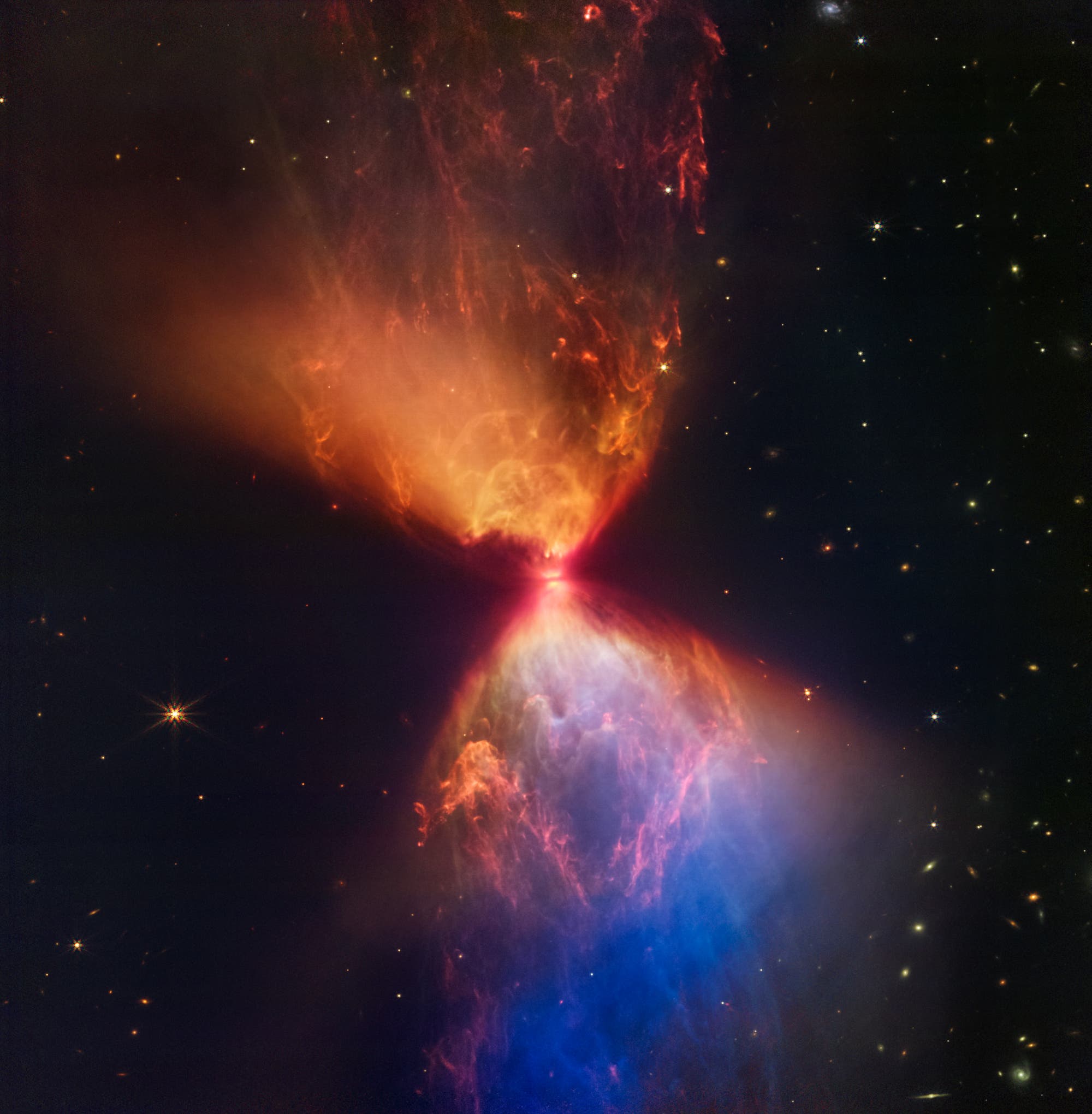 Ein Weltraumbild zeigt den Protostern L1527, umgeben von einer farbenfrohen Wolke aus Gas und Staub. Die Wolke hat eine sanduhrähnliche Form mit leuchtenden Orange- und Blautönen, die von einem hellen Zentrum ausgehen. Im Hintergrund sind zahlreiche Sterne vor einem dunklen Weltraum zu sehen. Dieses Bild veranschaulicht die Entstehung eines neuen Sterns und die dynamischen Prozesse in der frühen Phase der Sternentwicklung.