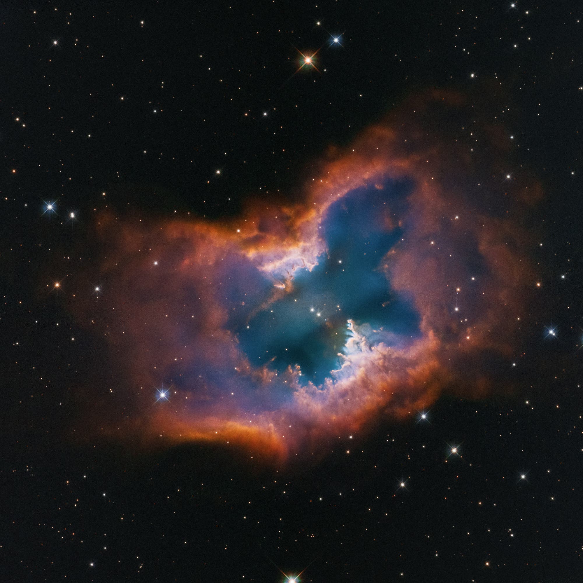 Ein atemberaubendes Bild des Weltraums zeigt den NGC 2899-Nebel, der wie ein Schmetterling geformt ist. Die leuchtenden Farben reichen von tiefem Blau im Zentrum bis zu leuchtendem Orange an den Rändern, umgeben von einem dunklen Sternenhintergrund. Zahlreiche kleine Sterne sind im gesamten Bild sichtbar. Dieses Bild vermittelt die Schönheit und Komplexität des Universums.