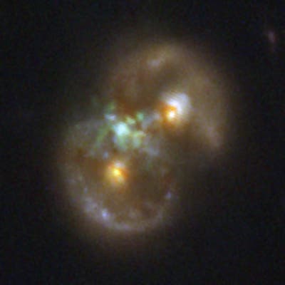 Das Bild zeigt eine Galaxie mit leuchtenden, diffusen Strukturen in verschiedenen Farben, darunter Grün, Gelb und Weiß, vor einem dunklen Hintergrund. Die Galaxie hat eine unregelmäßige Form und scheint mehrere helle Kerne zu haben. Es gibt keine sichtbaren Texte oder URLs im Bild. Das Bild zeigt eine Galaxie mit leuchtenden, diffusen Strukturen in verschiedenen Farben, darunter Grün, Gelb und Weiß, vor einem dunklen Hintergrund. Die Galaxie hat eine unregelmäßige Form und scheint mehrere helle Kerne zu haben. Es gibt keine sichtbaren Texte oder URLs im Bild.