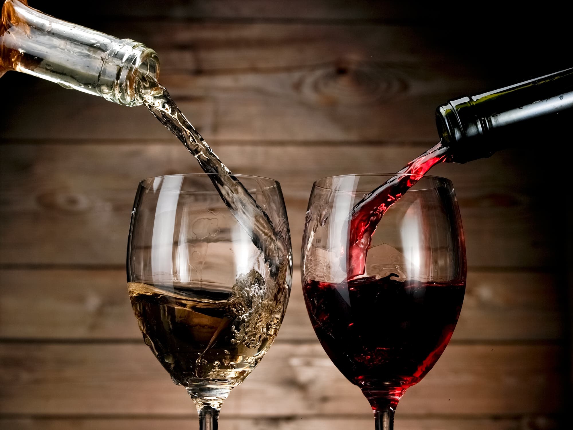 Rotwein und Weißwein werden aus der Flasche ins Glas eingeschenkt. 