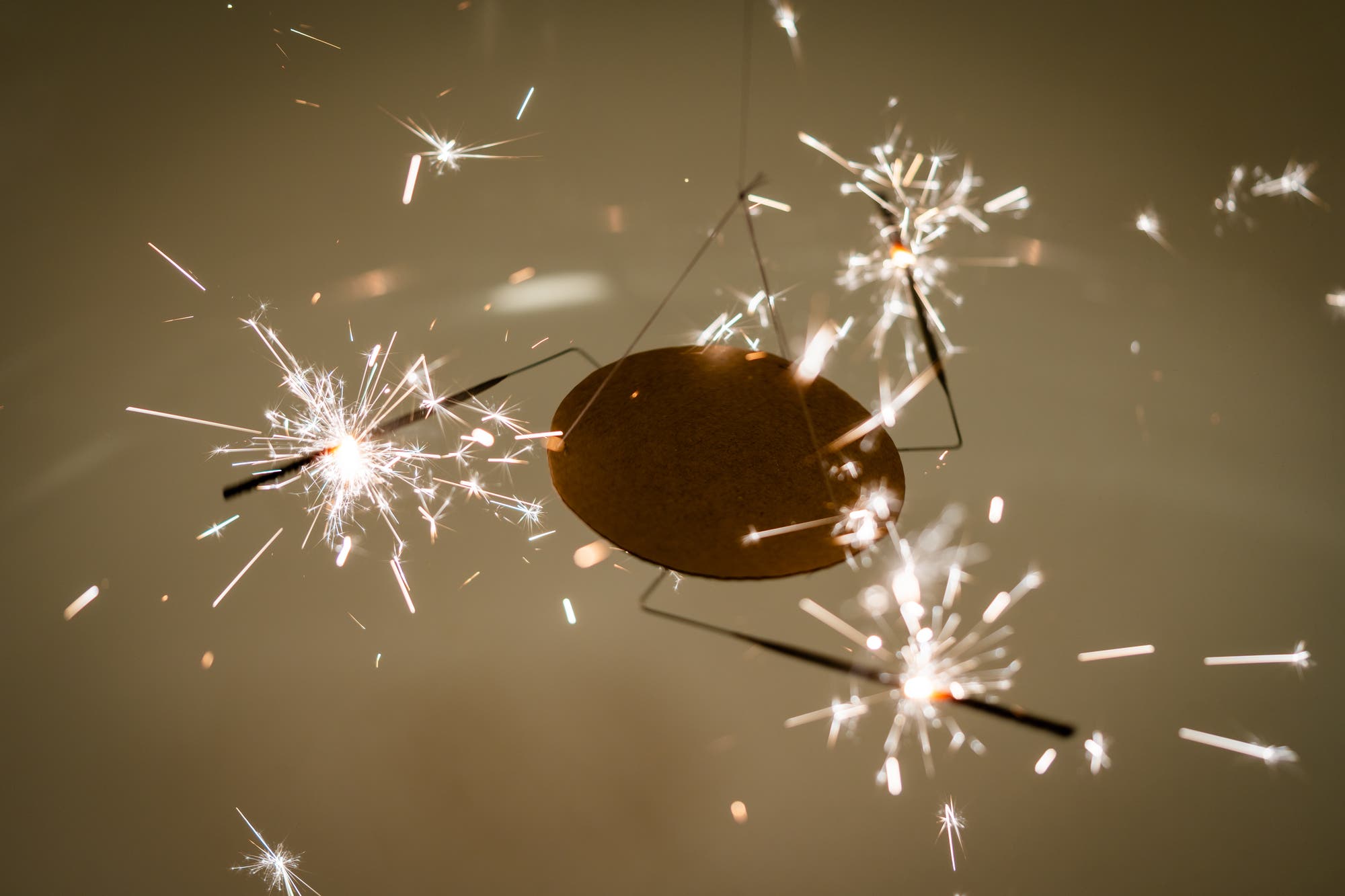 Drei brennende Wunderkerzen, die mit einem rechtwinklig geknickten Draht tangential an einer Scheibe aufgehängt sind, brennen mit sprühenden Funken.