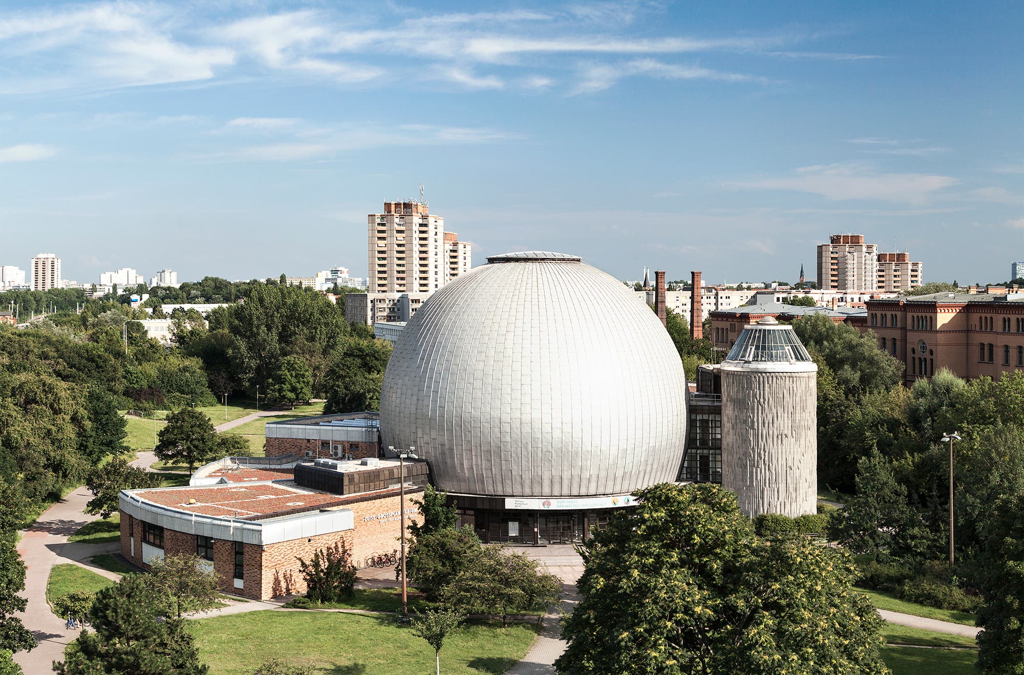 Das Gebäude des Zeiss-Großplanetariums Berlin mit seinem charakteristischen runden Dom ist vor dem Hintergrund einiger Gebäude zu sehen.