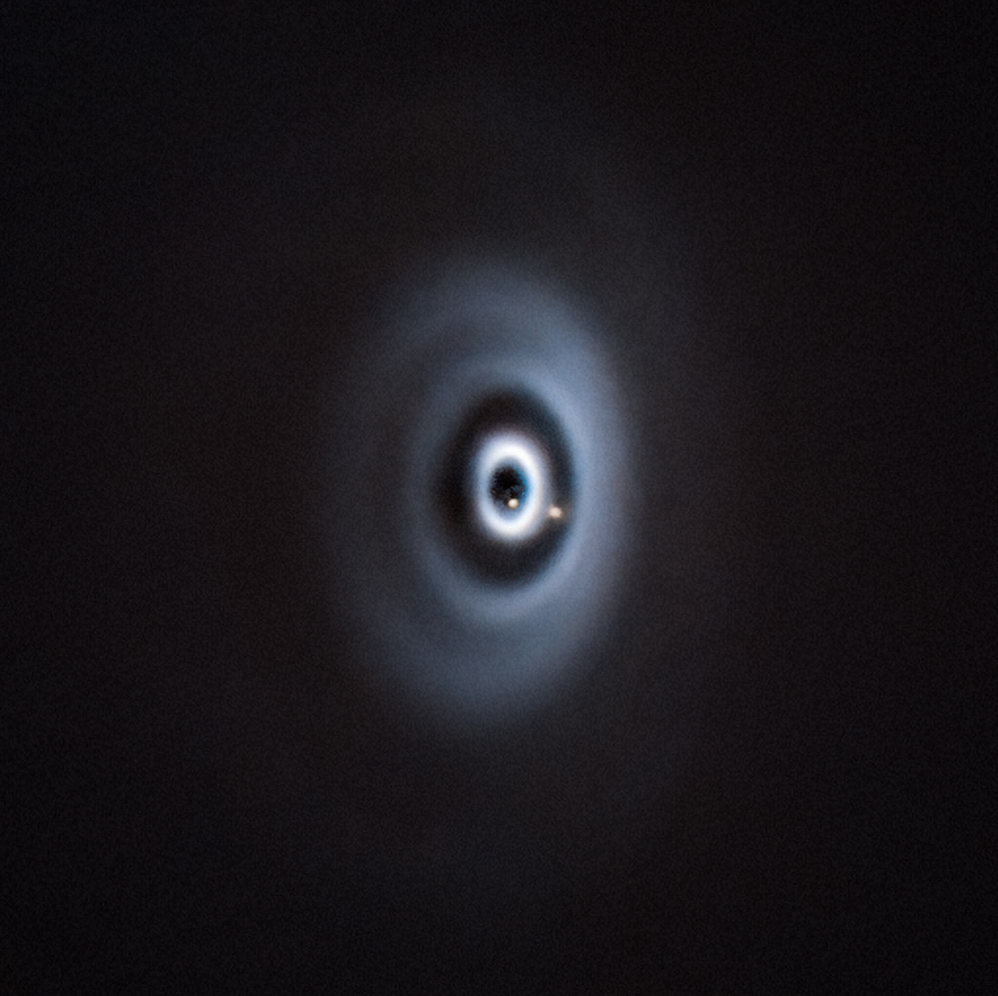 Ein astronomisches Bild zeigt eine zentrale Lichtquelle, umgeben von konzentrischen, leuchtenden Ringen auf dunklem Hintergrund. Diese Ringe weisen auf die Struktur einer protoplanetaren Scheibe oder eines &auml;hnlichen kosmischen Ph&auml;nomens hin. Die Darstellung hebt die Symmetrie und die leuchtenden Details der Ringe hervor, die sich von der Mitte nach au&szlig;en erstrecken.