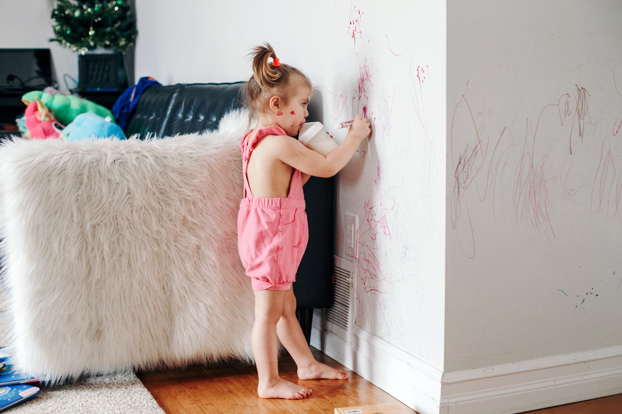 Ein kleines Mädchen bekritzelt versonnen die Wohnzimmerwand mit roter Farbe. 