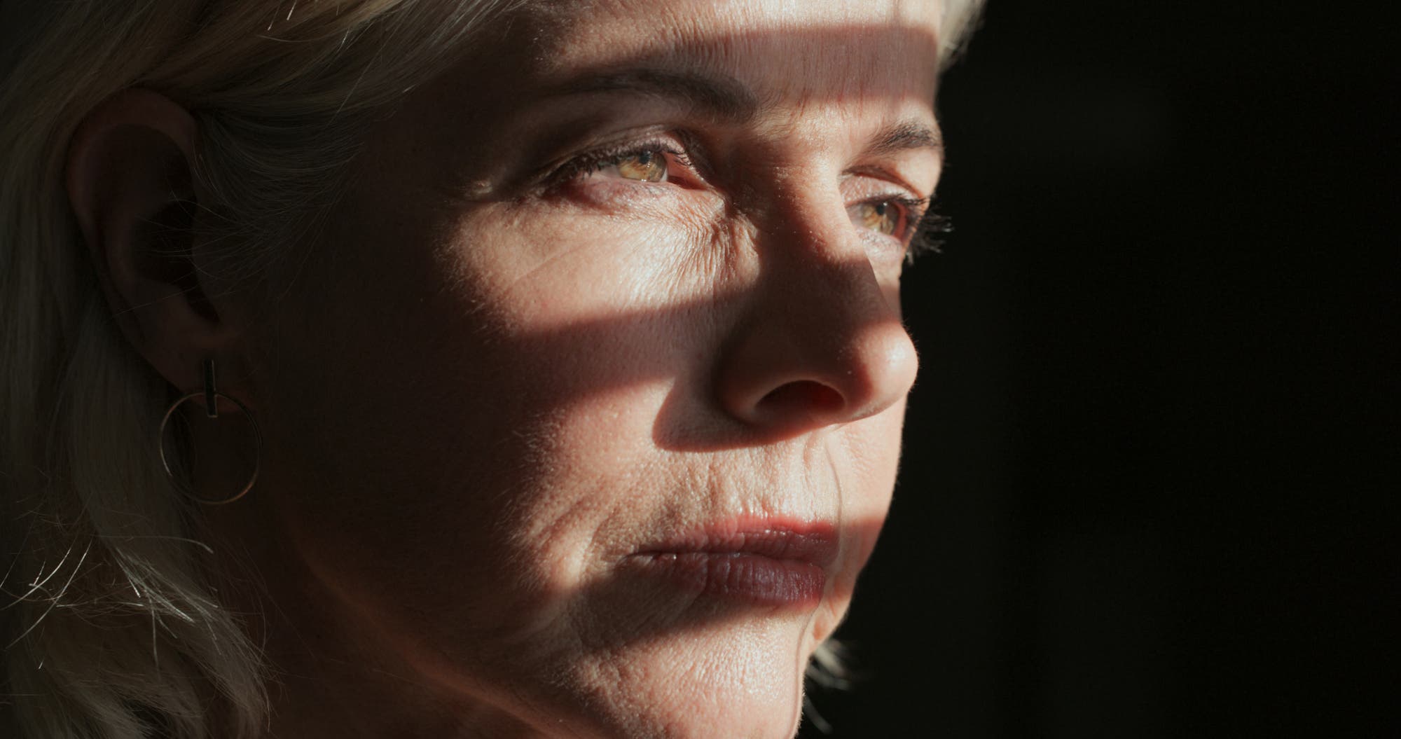 Gesicht einer ernst blickenden Frau in Großaufnahme, teilweise im Schatten, teilweise beleuchtet