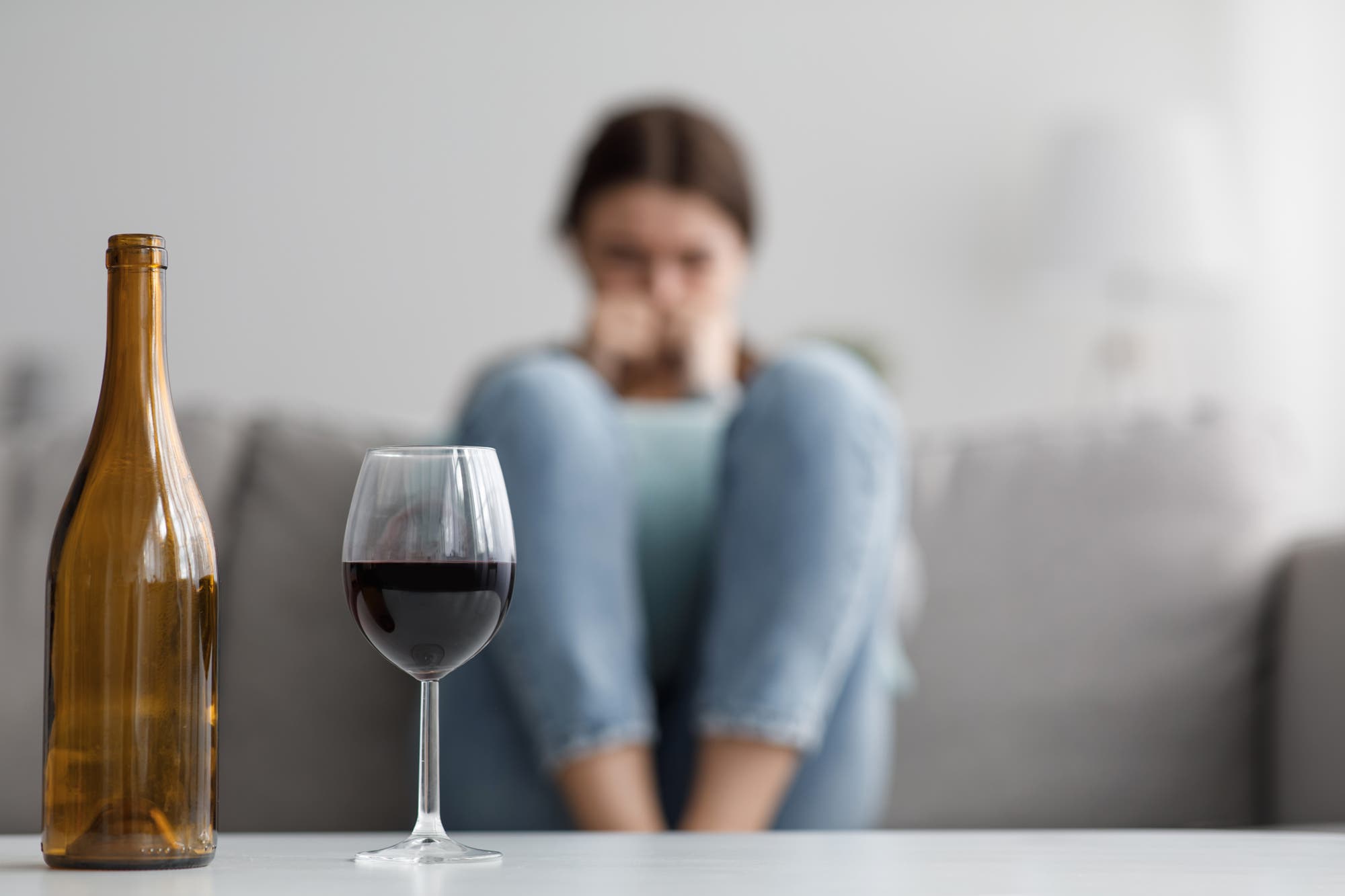 Hinter einer Flasche Wein mit Glas sitzt eine verzweifelt wirkende Frau