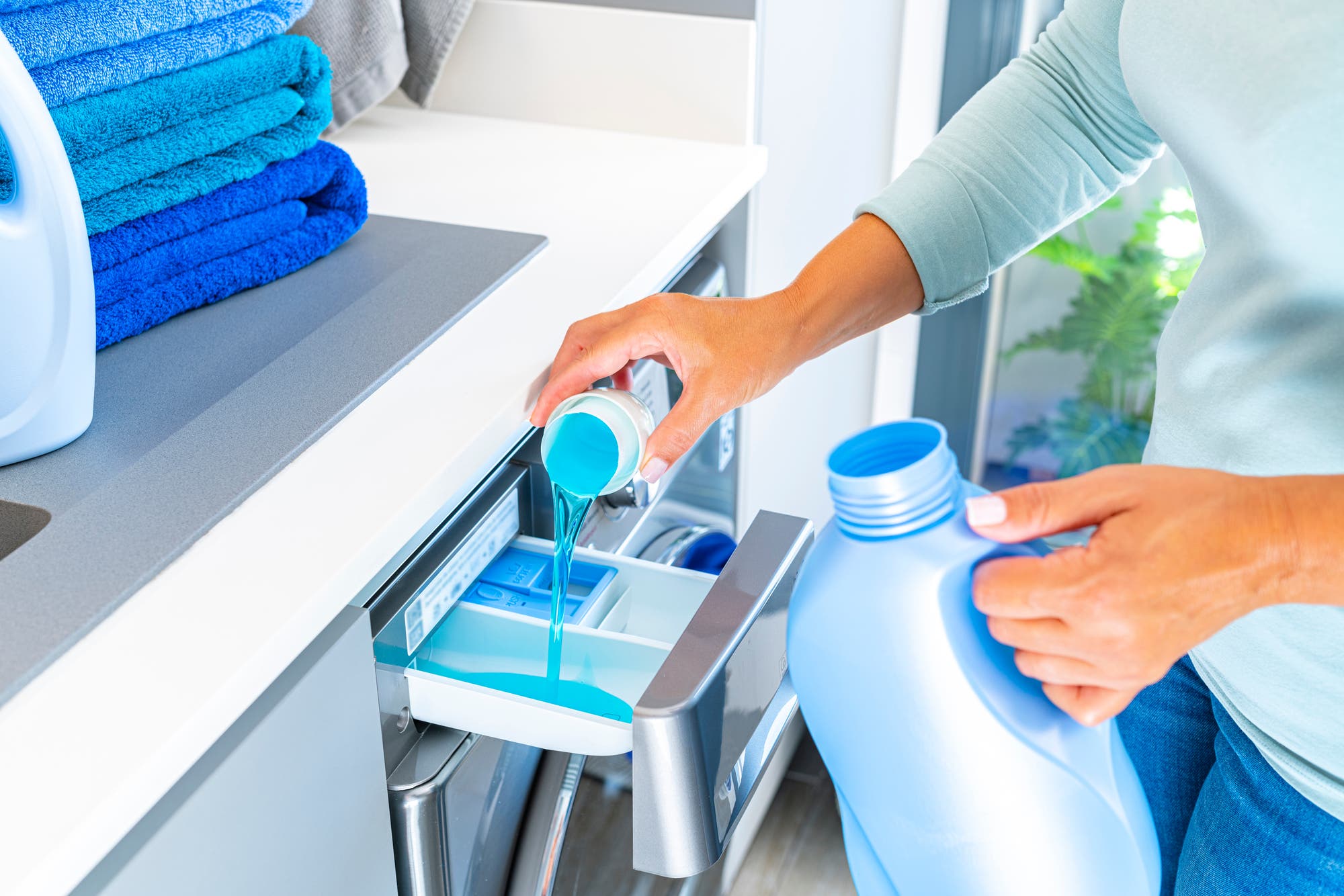Eine Frau kippt Waschmittel in das Fach einer Waschmaschine.