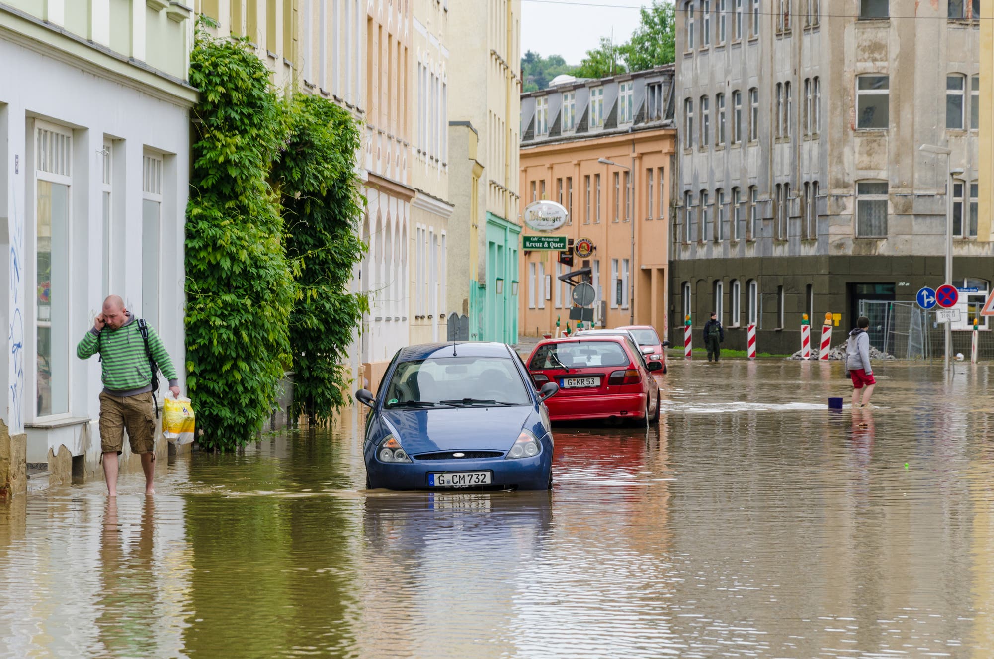 Überschwemmte Straße mit im Wasser stehenden Autos und vermutlich vollgelaufenen Kellern.