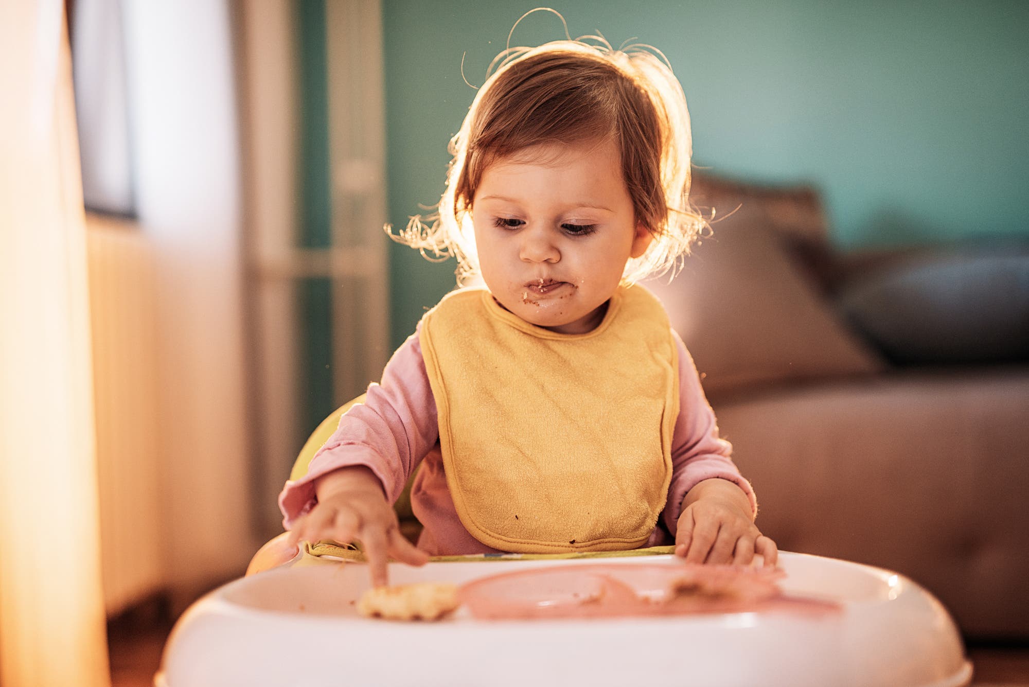 Ein kleines Mädchen hat ein Lätzchen um und stochert mit ihrem Finger skeptisch in ihrem Essen herum.