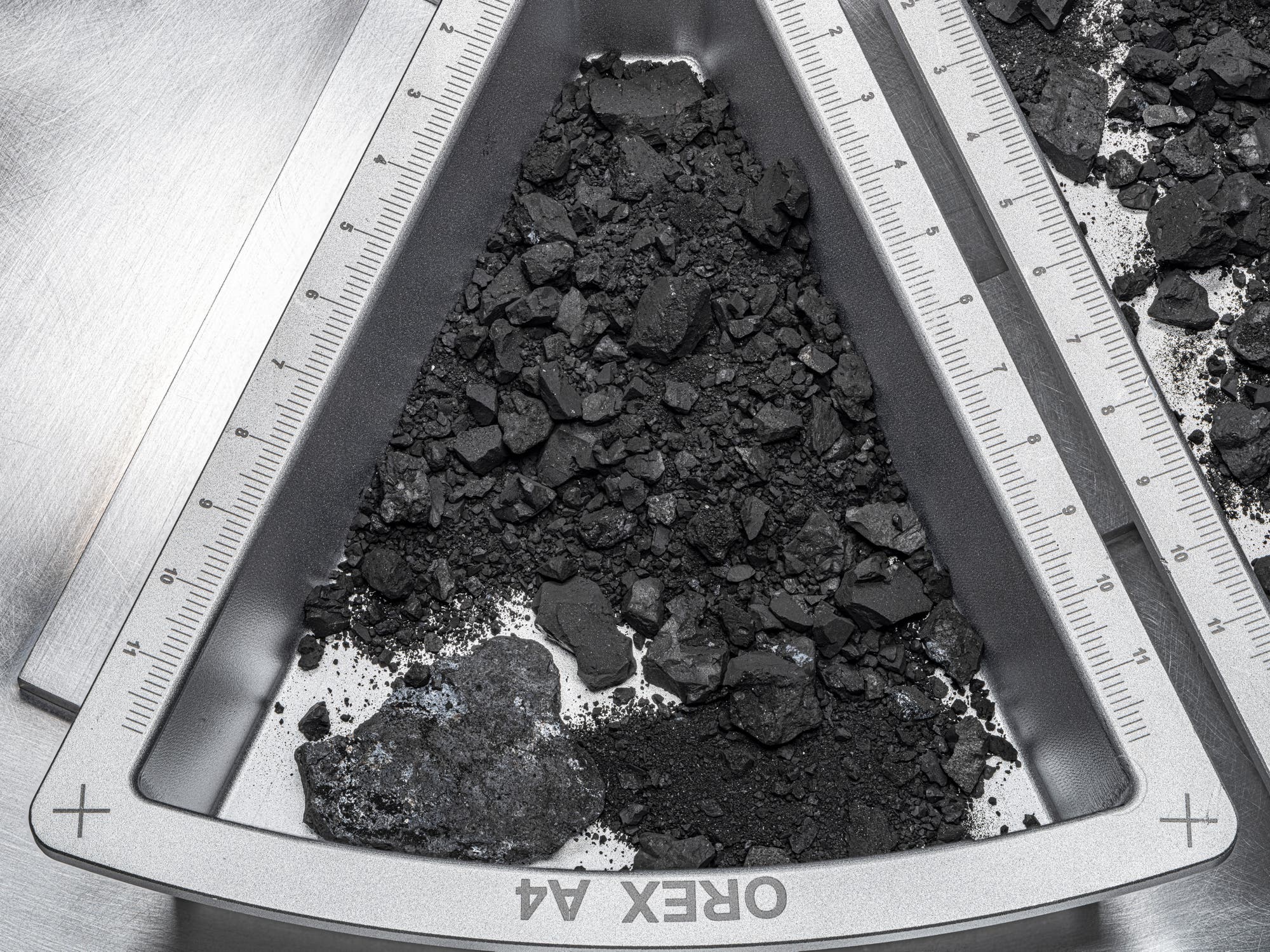 In einem Behältnis, in das ein Teil des Probenmaterials von Asteroid Bennu überführt wurde, lassen sich feinste Körnchen erkennen