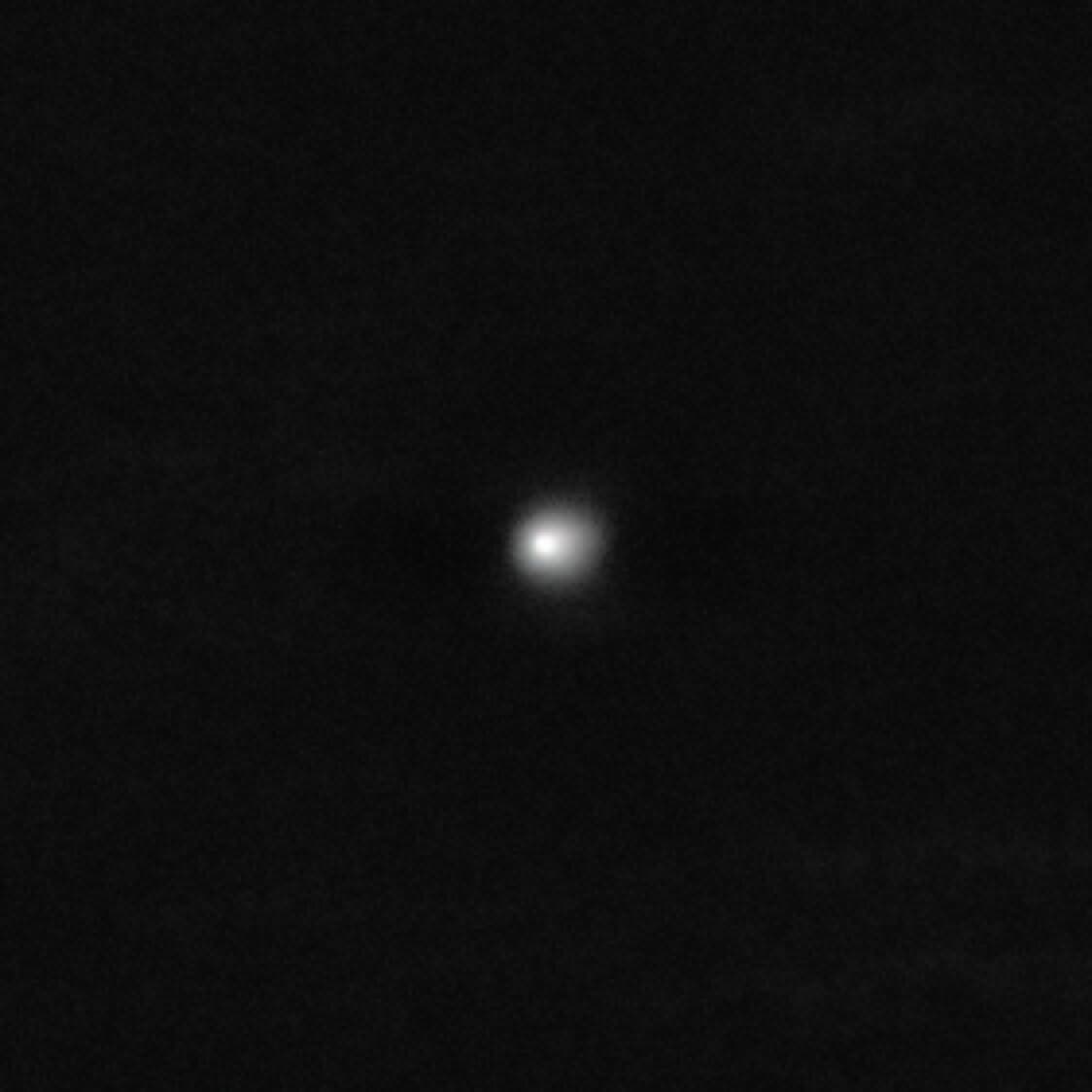 Ein unscharfer, heller Punkt in der Mitte eines ansonsten dunklen Bildes. Der Punkt hebt sich deutlich vom schwarzen Hintergrund ab und ist der interstellare Komet 3I/ATLAS. Es gibt keine weiteren erkennbaren Details oder Textelemente im Bild.