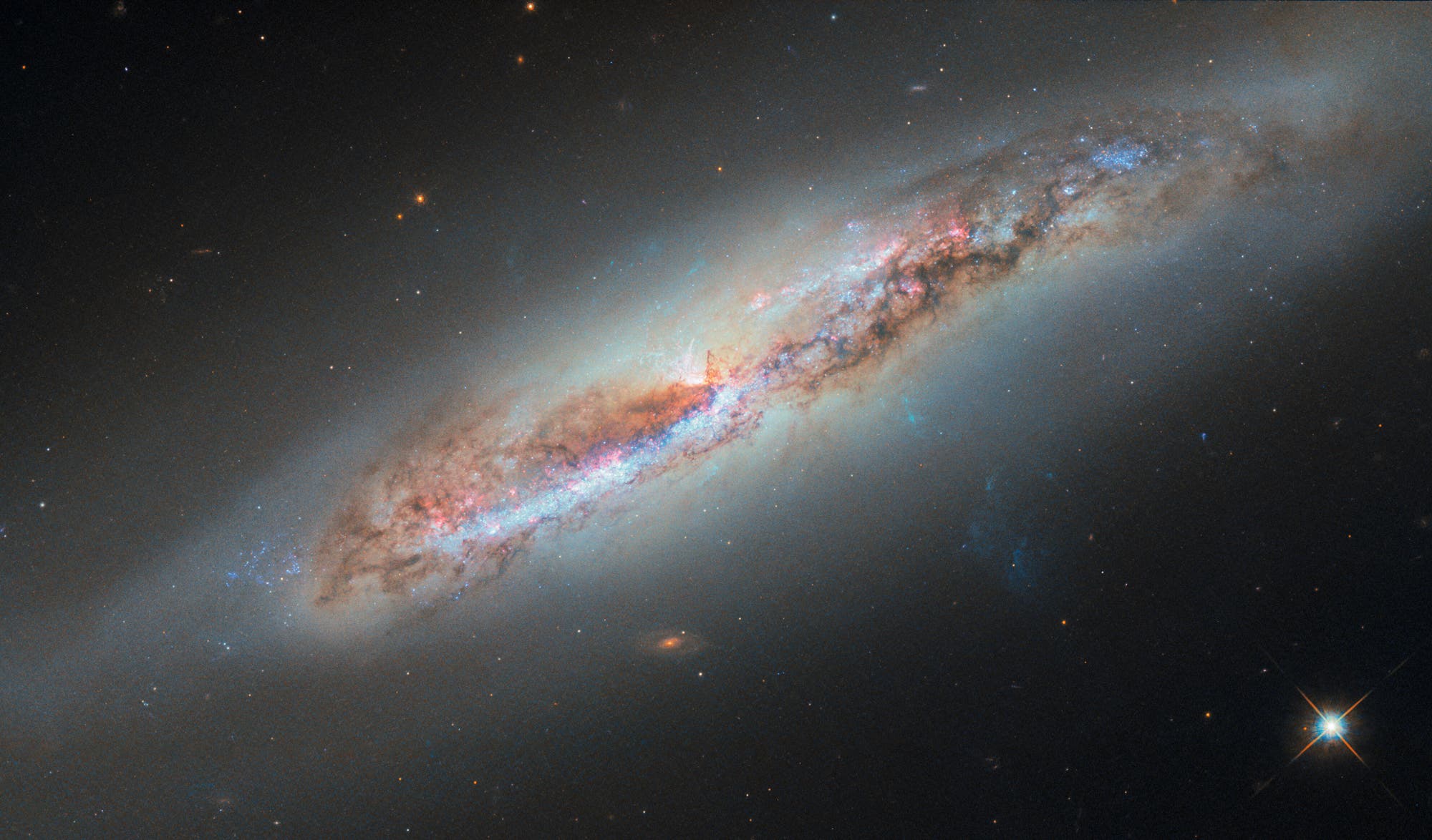 Eine Spiralgalaxie im Weltraum, die sich diagonal durch das Bild erstreckt. Die Galaxie zeigt leuchtende Farben in Blau, Rosa und Weiß, die auf Sternentstehungsgebiete hinweisen. Umgeben von einem dunklen Hintergrund mit verstreuten Sternen und Galaxien. Die Struktur der Galaxie ist detailliert sichtbar, mit einem hellen Kern und ausgedehnten Spiralarmen. Ein schwacher Schweif aus gas ist erkennbar, der aus dem Galaxienkern auszutreten scheint. Eine Spiralgalaxie im Weltraum, die sich diagonal durch das Bild erstreckt. Die Galaxie zeigt leuchtende Farben in Blau, Rosa und Weiß, die auf Sternentstehungsgebiete hinweisen. Umgeben von einem dunklen Hintergrund mit verstreuten Sternen und Galaxien. Die Struktur der Galaxie ist detailliert sichtbar, mit einem hellen Kern und ausgedehnten Spiralarmen. Ein schwacher Schweif aus gas ist erkennbar, der aus dem Galaxienkern auszutreten scheint.