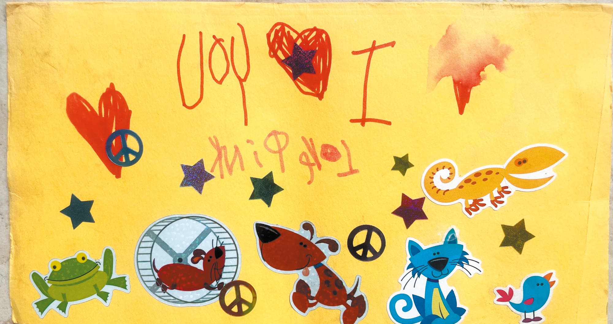 Kinderzeichnung mit Spiegelschrift und Tierstickern auf gelbem Hintergrund
