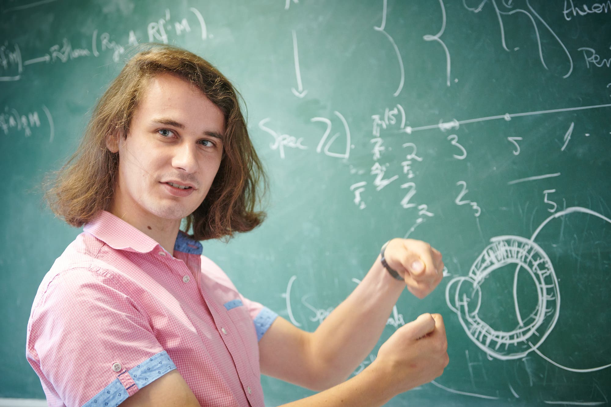 Der Mathematiker Peter Scholze steht gestikulierend vor einer Tafel mit mathematischen Formeln
