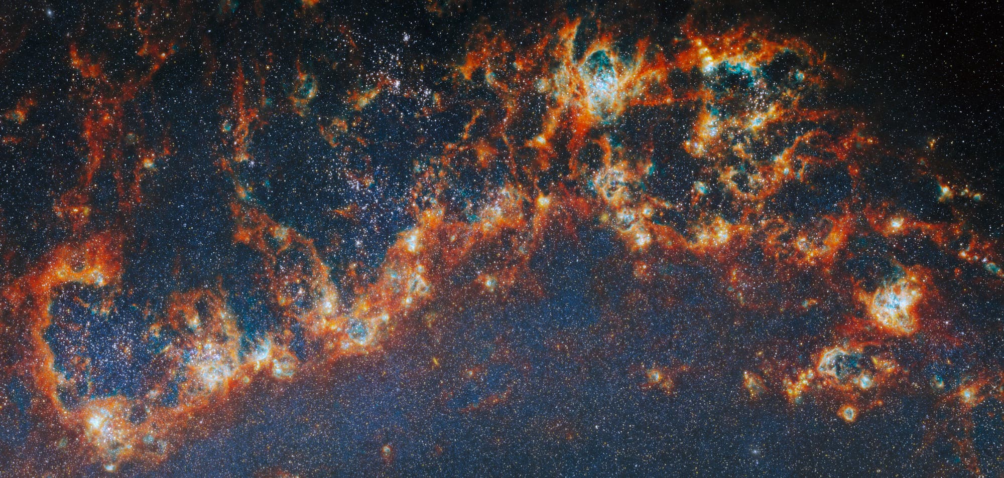 Das Bild zeigt eine detaillierte Aufnahme einer Galaxie mit leuchtenden Gaswolken und unz&auml;hligen Sternen. Die Farben reichen von tiefem Blau bis zu leuchtendem Orange und Rot, was auf verschiedene chemische Zusammensetzungen und Temperaturen hinweist. Die Struktur der Gaswolken ist komplex und filamentartig, was auf aktive Sternentstehungsprozesse hindeutet. Der Hintergrund ist mit vielen kleinen, funkelnden Sternen &uuml;bers&auml;t, die die Weite des Universums verdeutlichen.