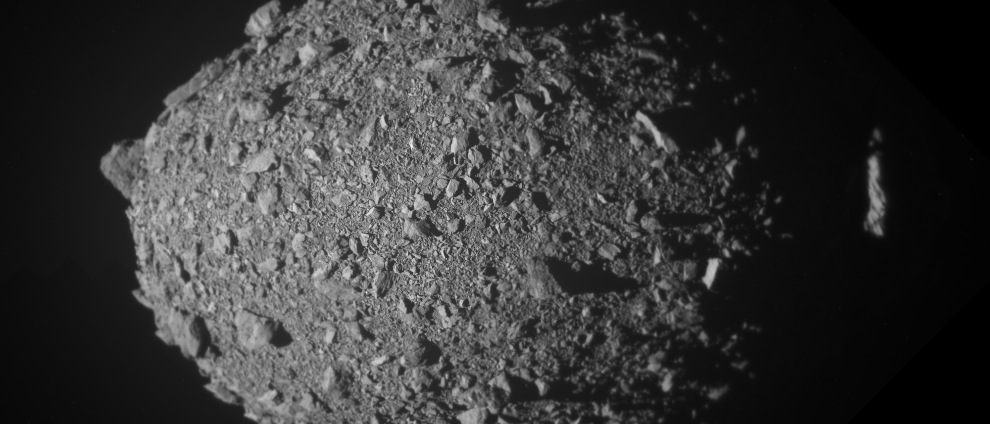 In diesem aus mehreren Bildern zusammengesetzten Bild ist der Asteroidenmond Dimorphos kurz vor dem Aufprall der DART-Sonde zu sehen. Der Asteroid ähnelt einem eierförmigen, losen Schutthaufe aus kleinen Steinen und Geröll. Die Aufnahme ist in schwarz/weiß.