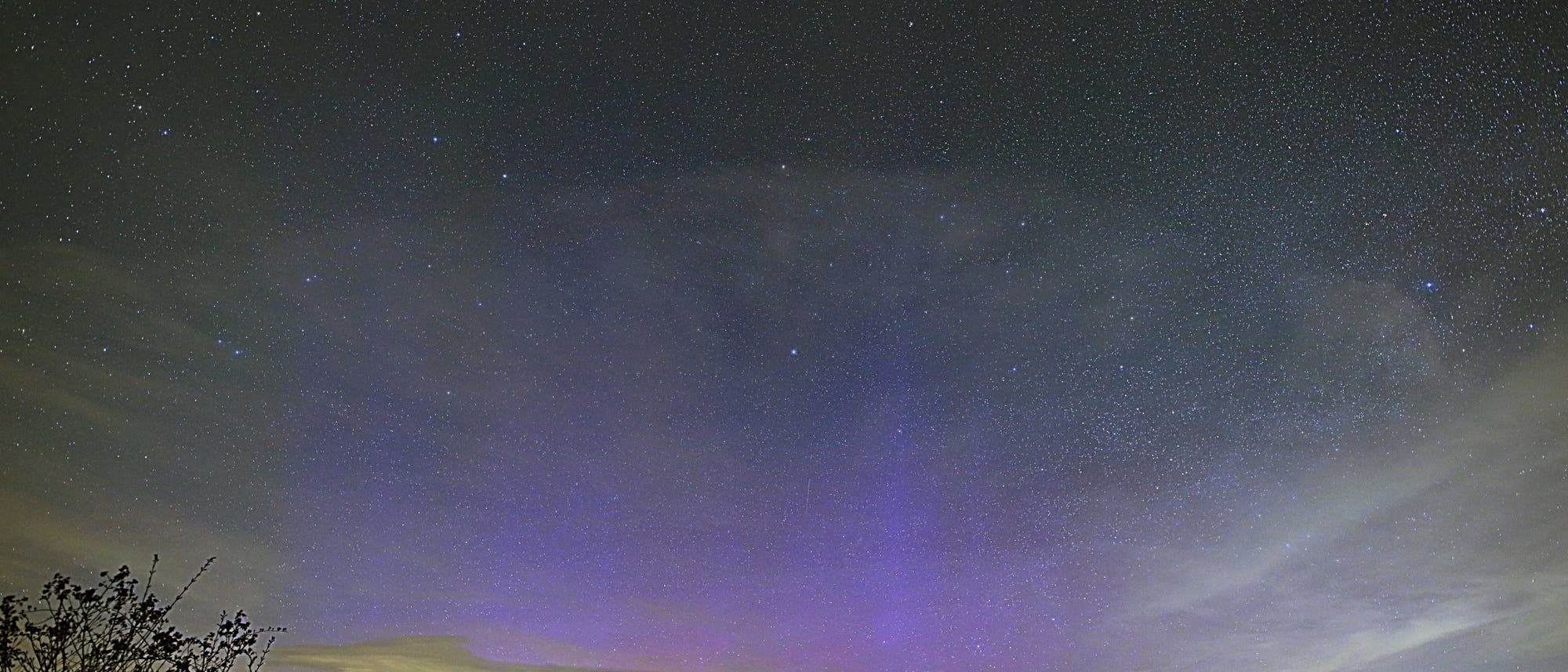 Am Nachthimmel ist ein großflächiges blaues Licht zu sehen, kleinere Bereiche sind auch magentafarben. Einzelne Sterne sind in den nachtschwarzen Bereichen des Himmels erkennbar.