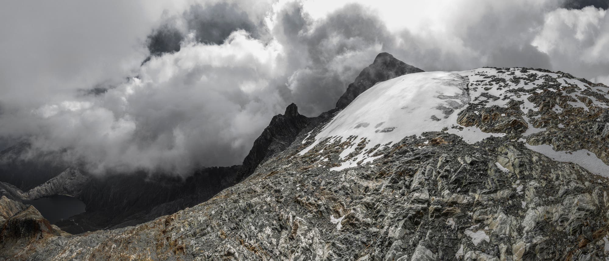 Archivbild des Humboldt-Gletschers in Venezuela, als dieser noch als Gletscher galt: eine kleine weiße Eisfläche in der rechten Bildmitte, umgeben von grauem Gestein. Im Hintergrund ist ein Berggipfel, der von weißen Wolken umgeben wird.
