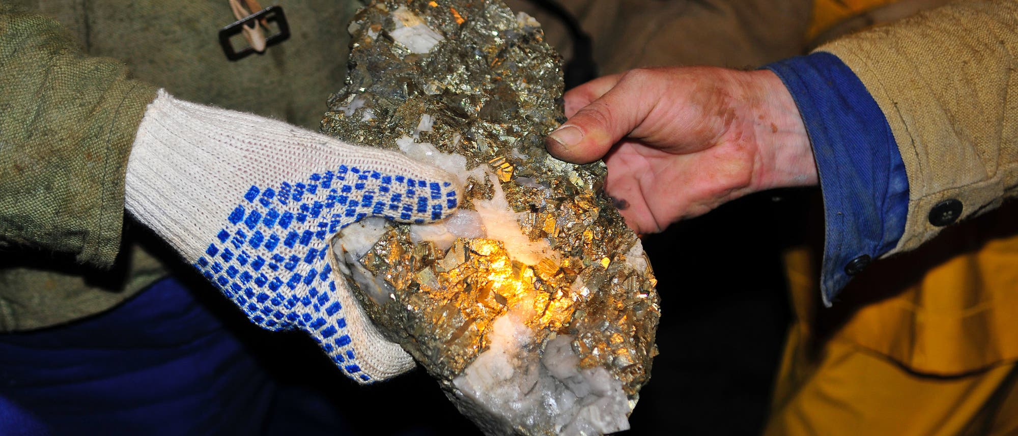 Bergleute halten einen mit Gold überzogenen Erzbrocken in die Kamera.