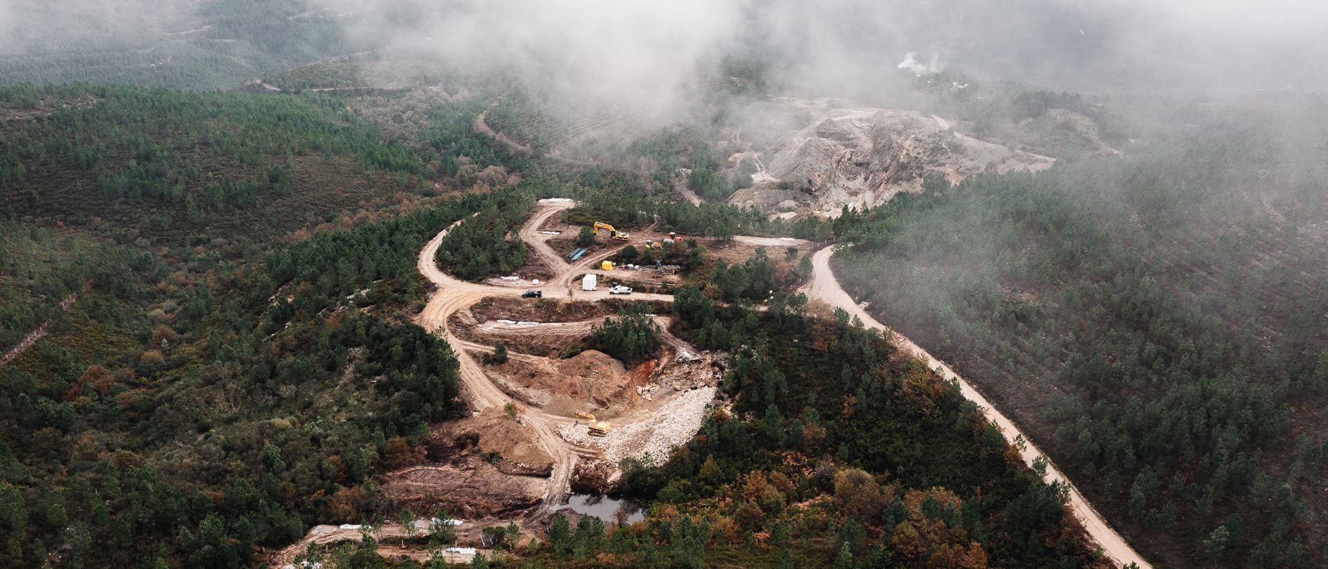 Eine Luftaufnahme zeigt eine Waldlandschaft, in deren Mitte eine Mine ausgebaggert wird.